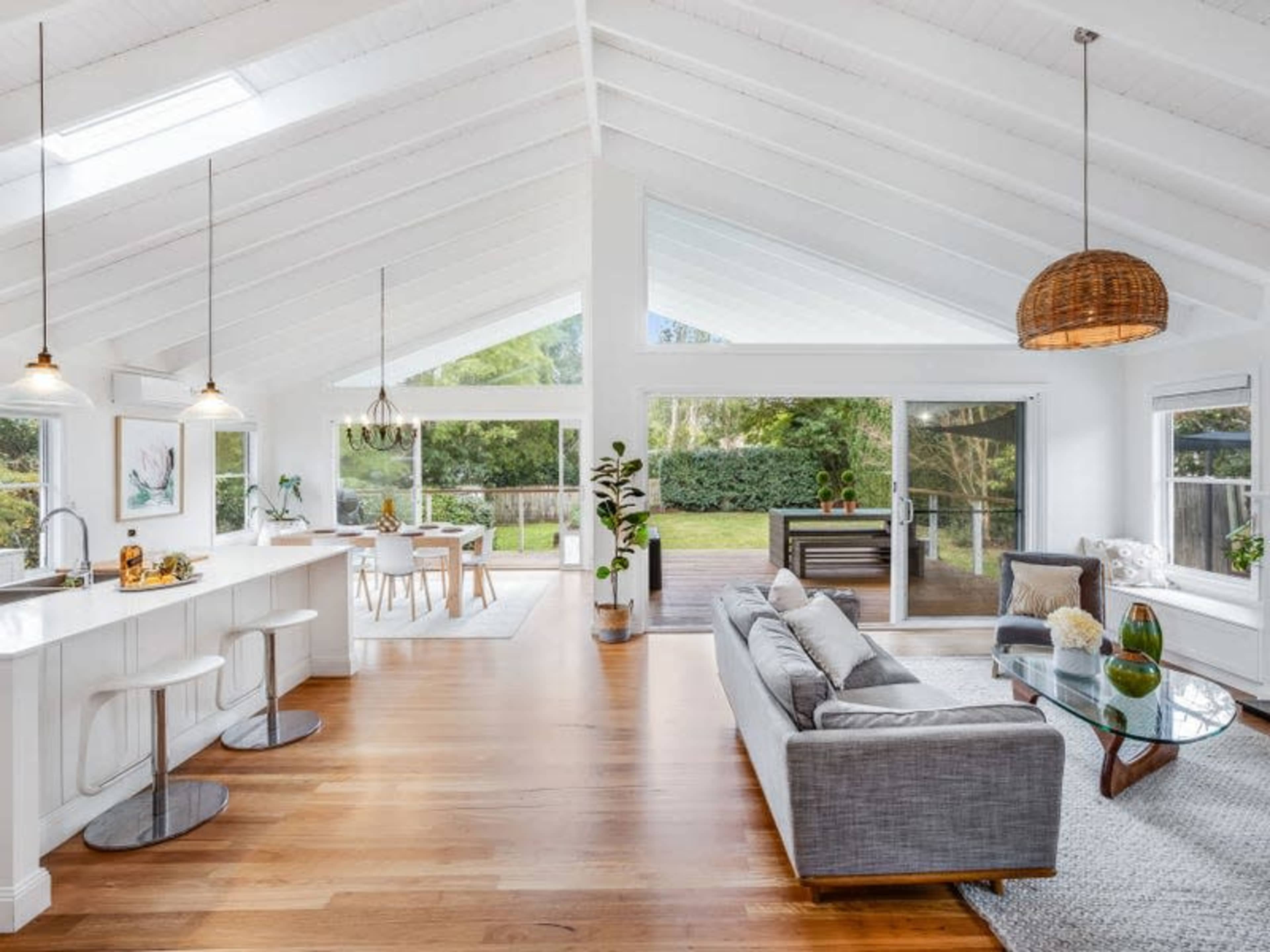 A spacious, open-concept living area features high ceilings, a modern kitchen with bar stools, and large windows that let in natural light.