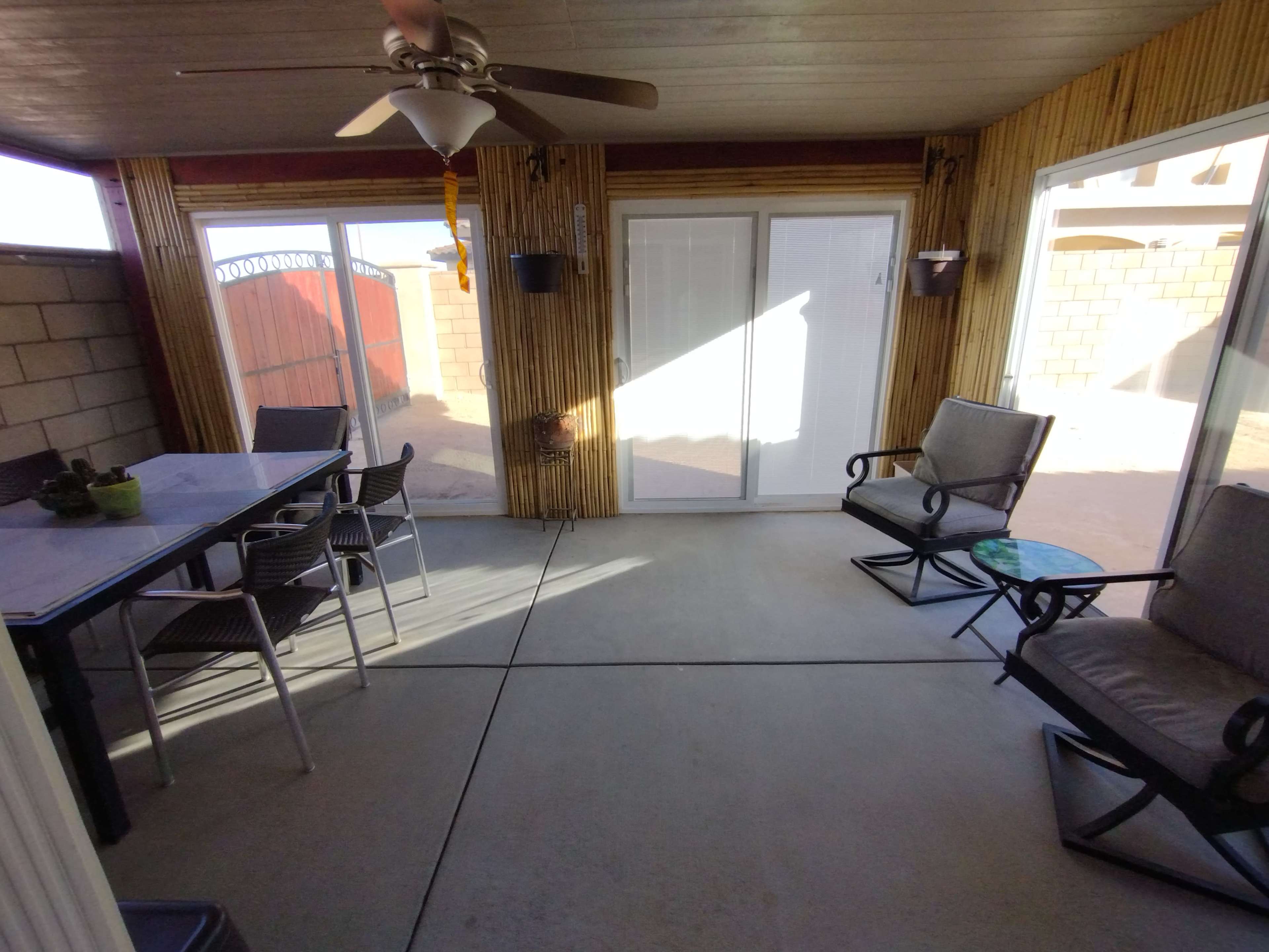 A screened-in porch furnished with a table and chairs, two rocking chairs, and bamboo accents on the walls.