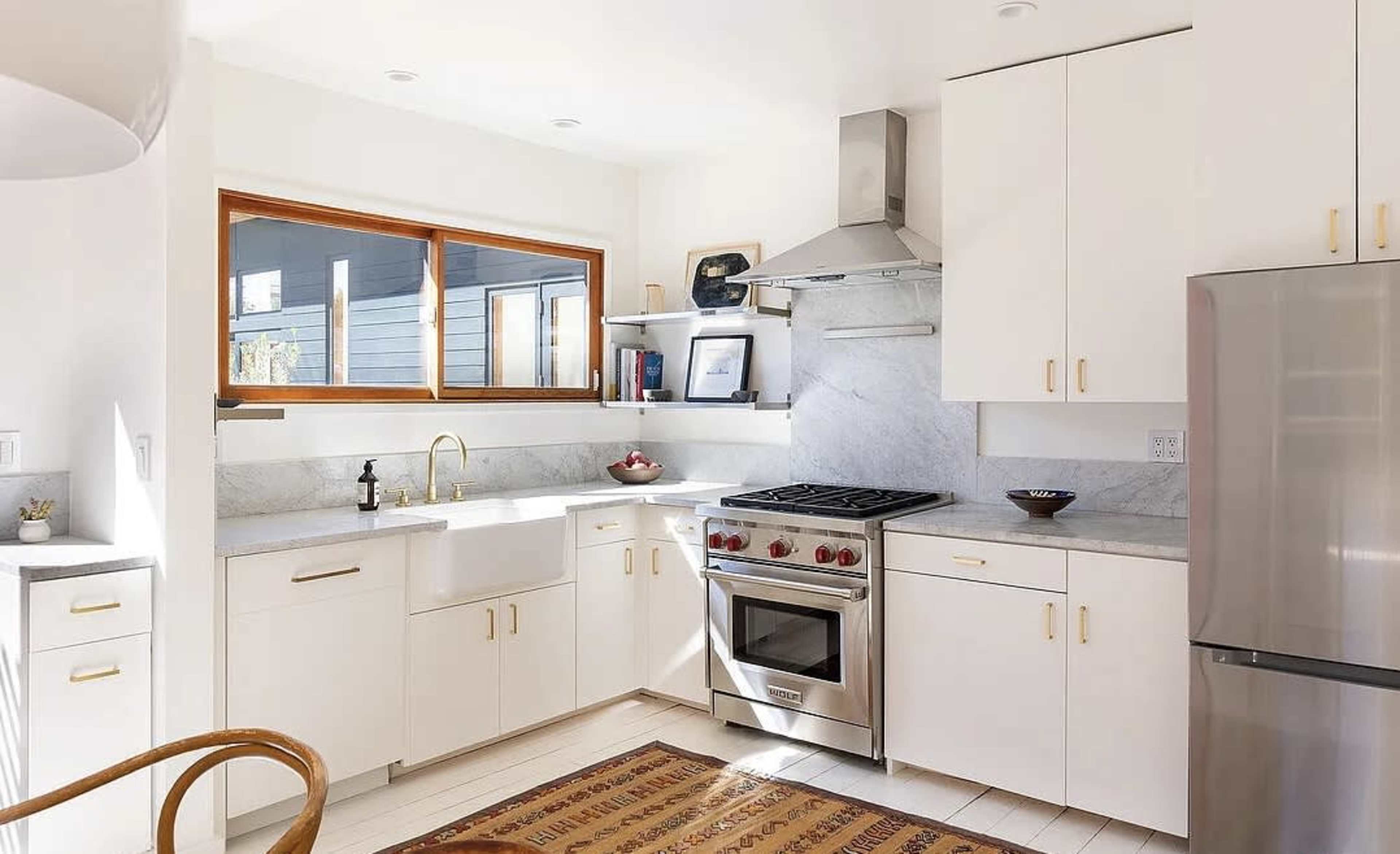 The image shows a modern kitchen featuring white cabinetry, a stainless steel refrigerator, a gas stove with an oven, and a stone countertop.