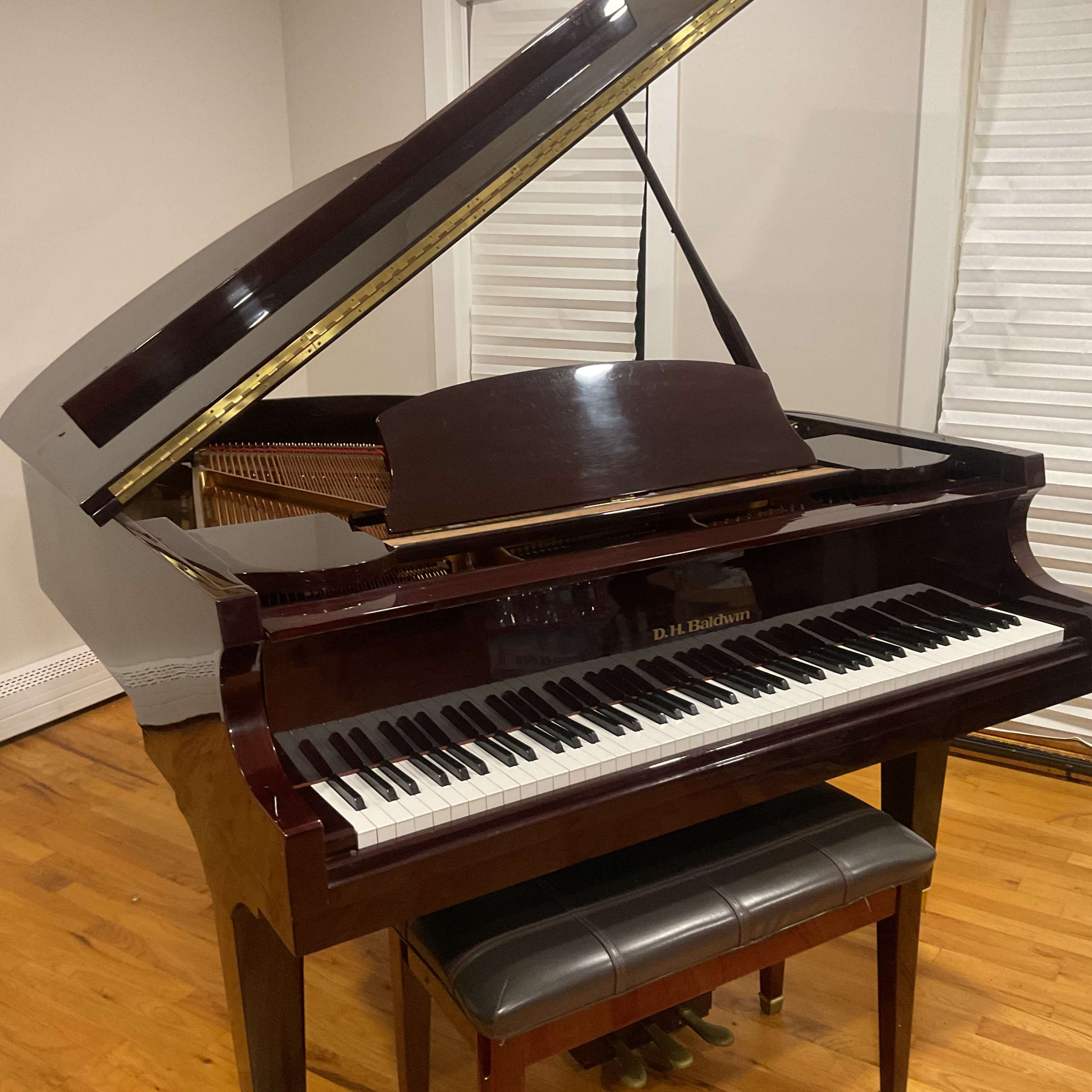 A polished grand piano is positioned in a room with wooden floors and light-colored walls.