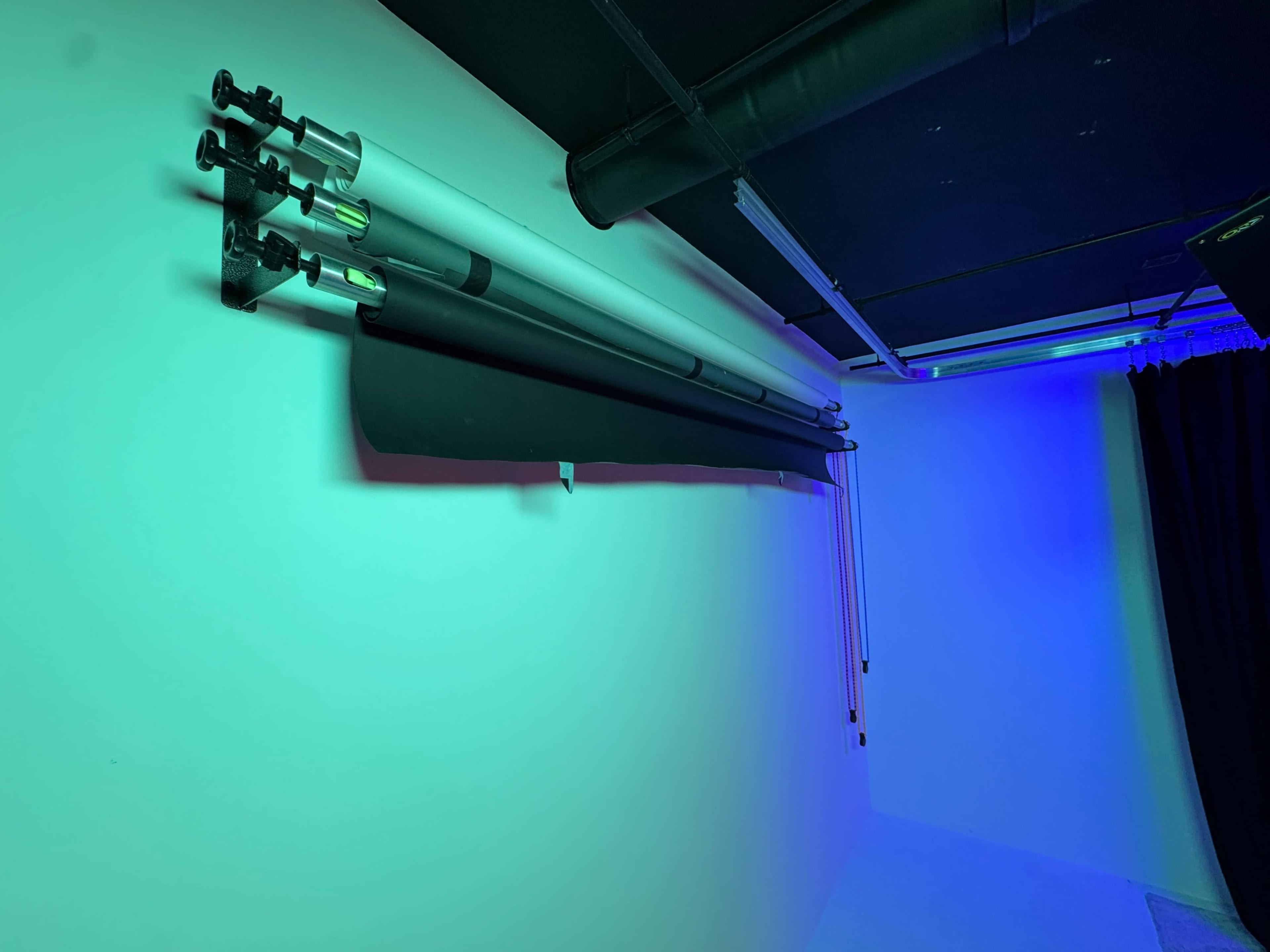 The image shows a setup featuring several photography backdrop rolls mounted on a wall under green lighting, with a curtain in the background.