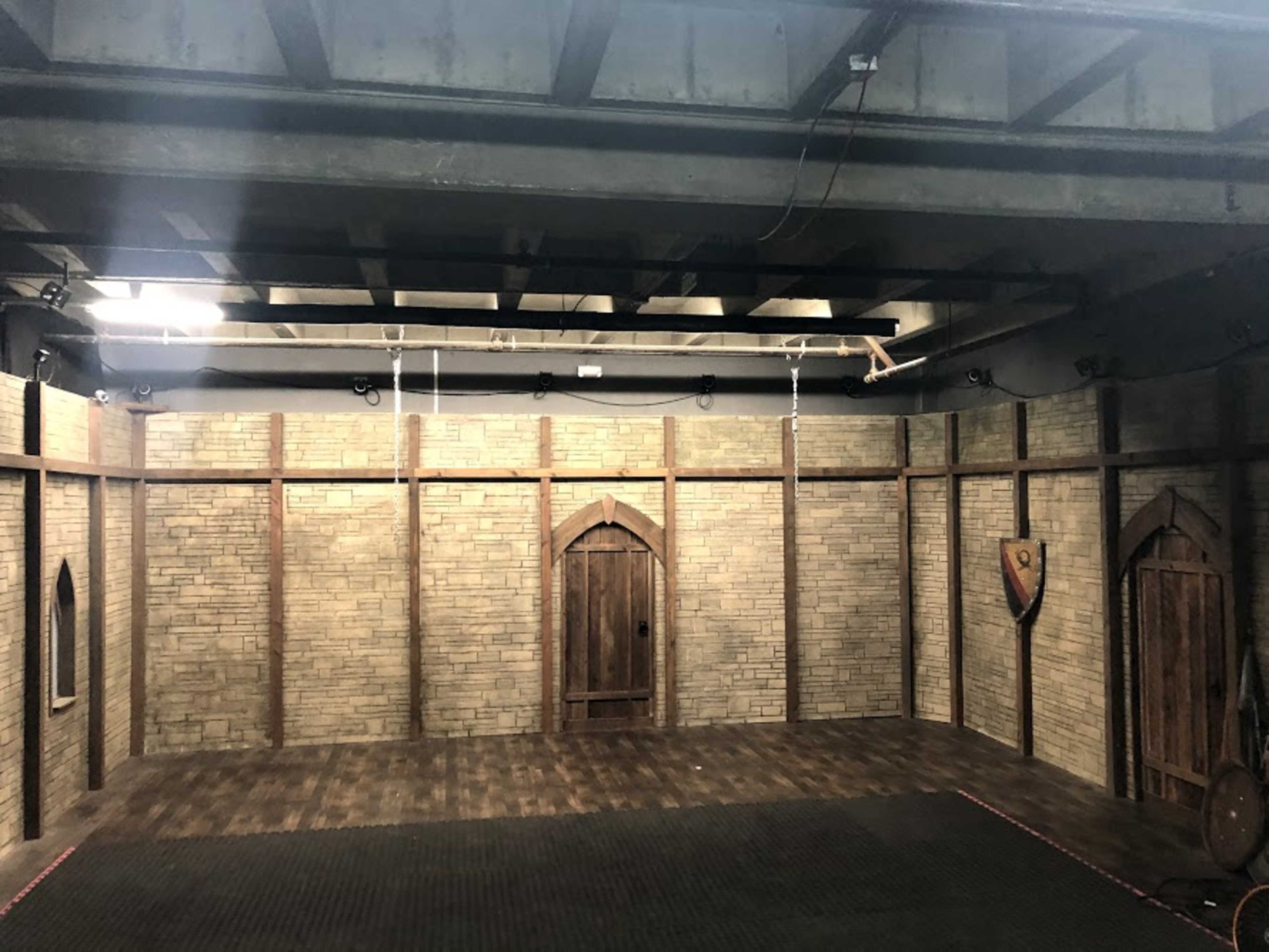 An empty room with brick walls, wooden trim, a central wooden door, and various light fixtures hanging from the ceiling.