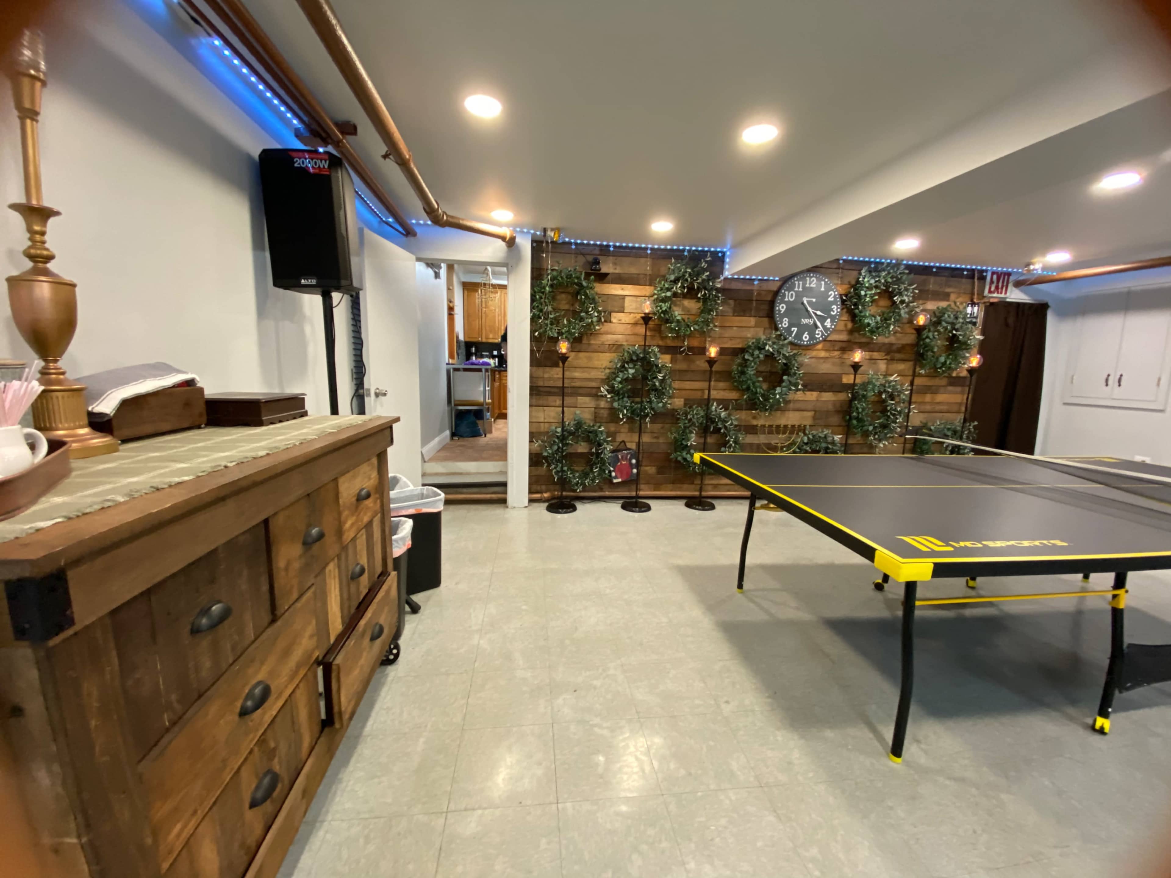 A recreation room featuring a ping pong table, a wooden cabinet, and decorated walls with greenery and a wall clock.