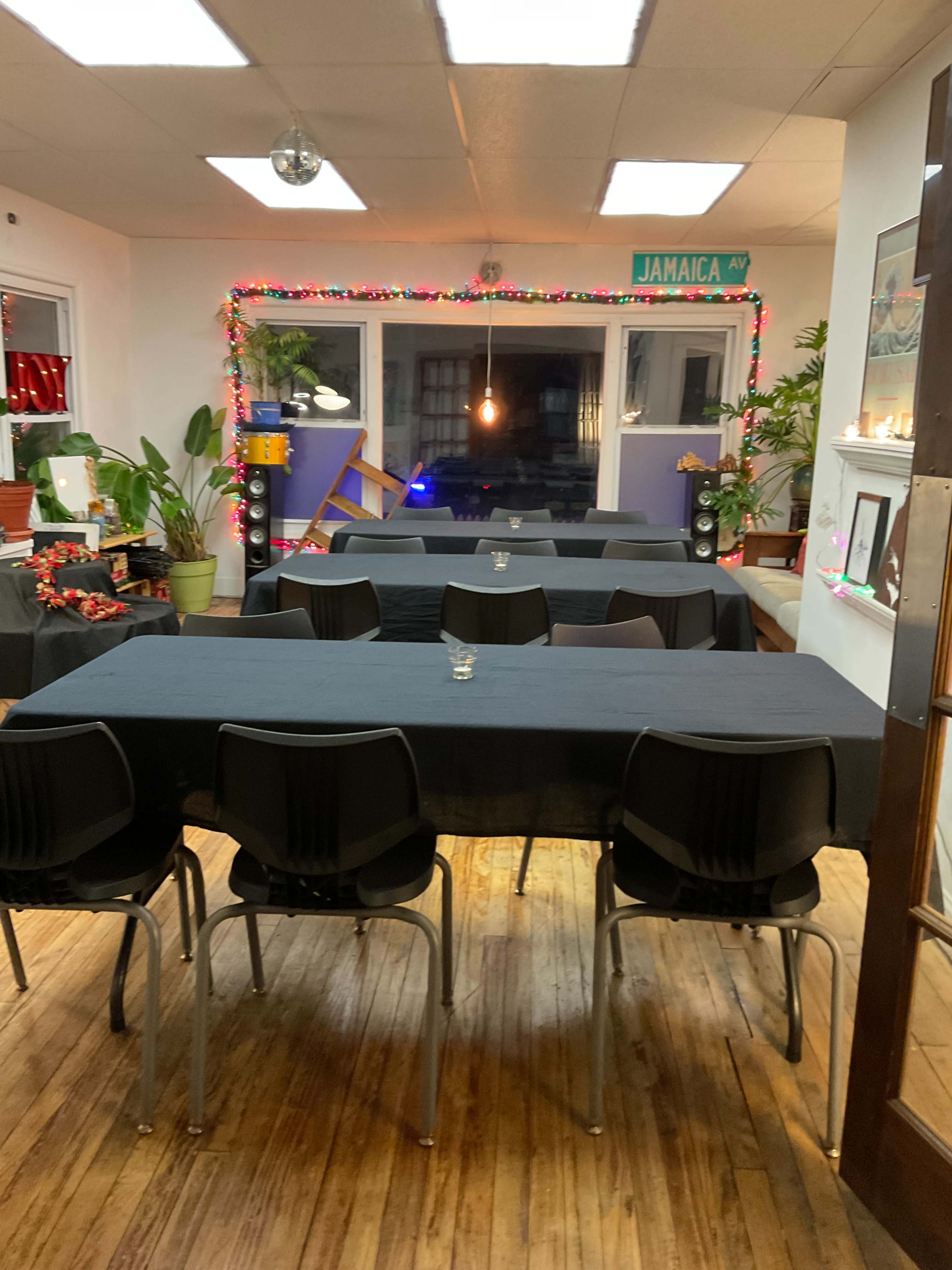 The image shows a dining area with black tablecloths covering several tables and chairs arranged neatly, adorned with decorative lights and plants.
