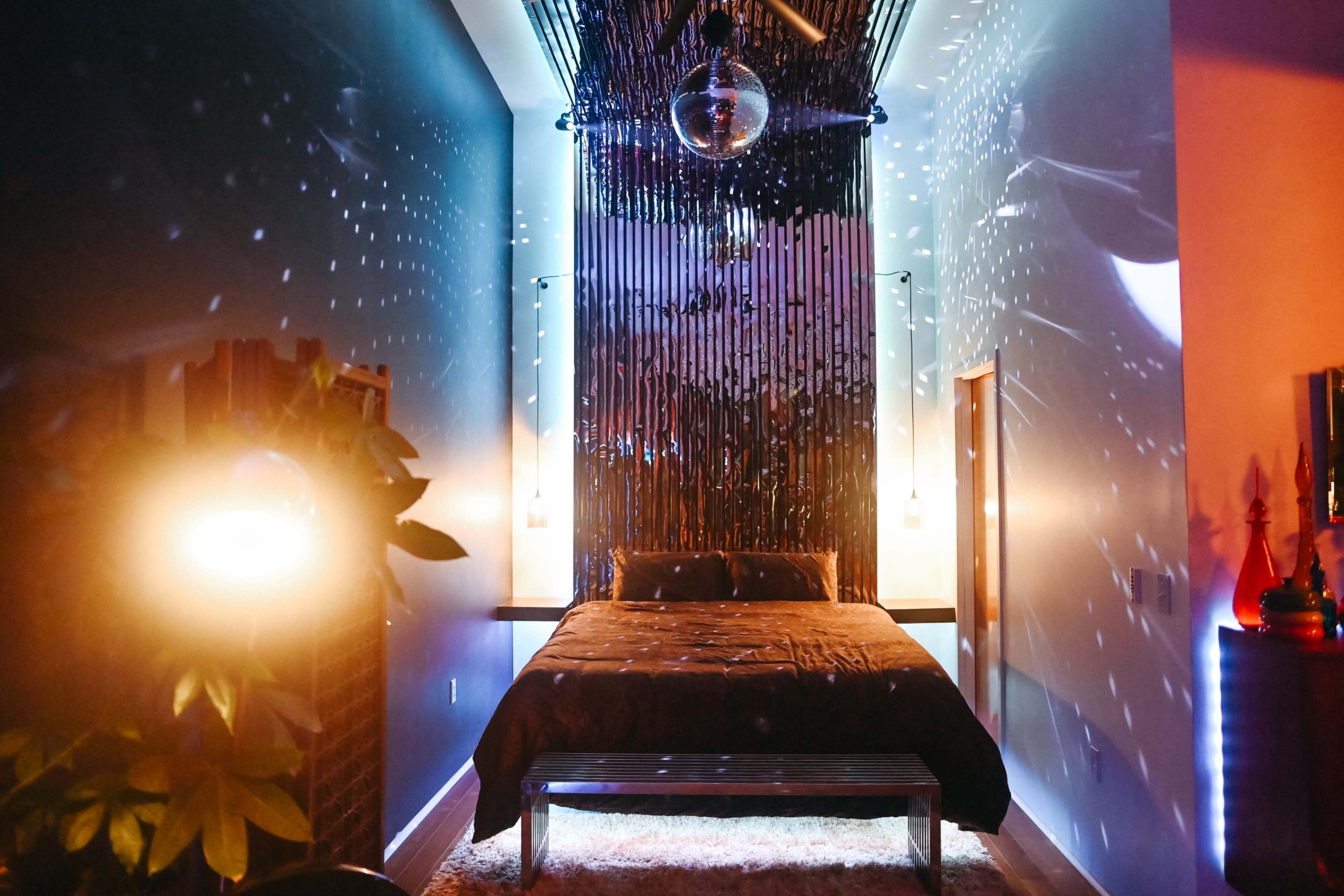 A dimly lit bedroom with a bed centered against a wall and decorative lighting casting reflections on the walls.
