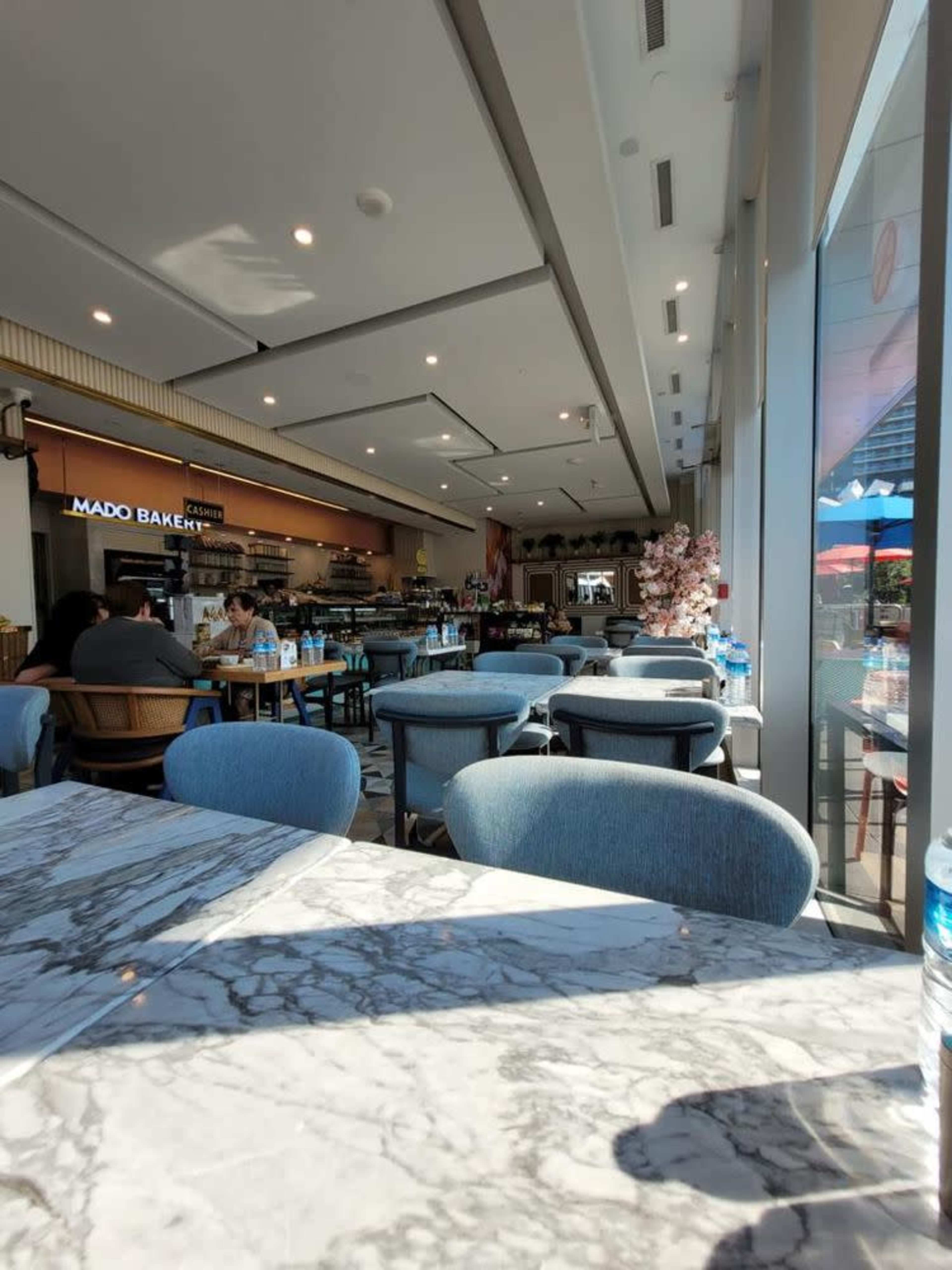 The image shows the interior of a café with a marble table, blue upholstered chairs, and patrons seated in the background, while a counter displays baked goods.