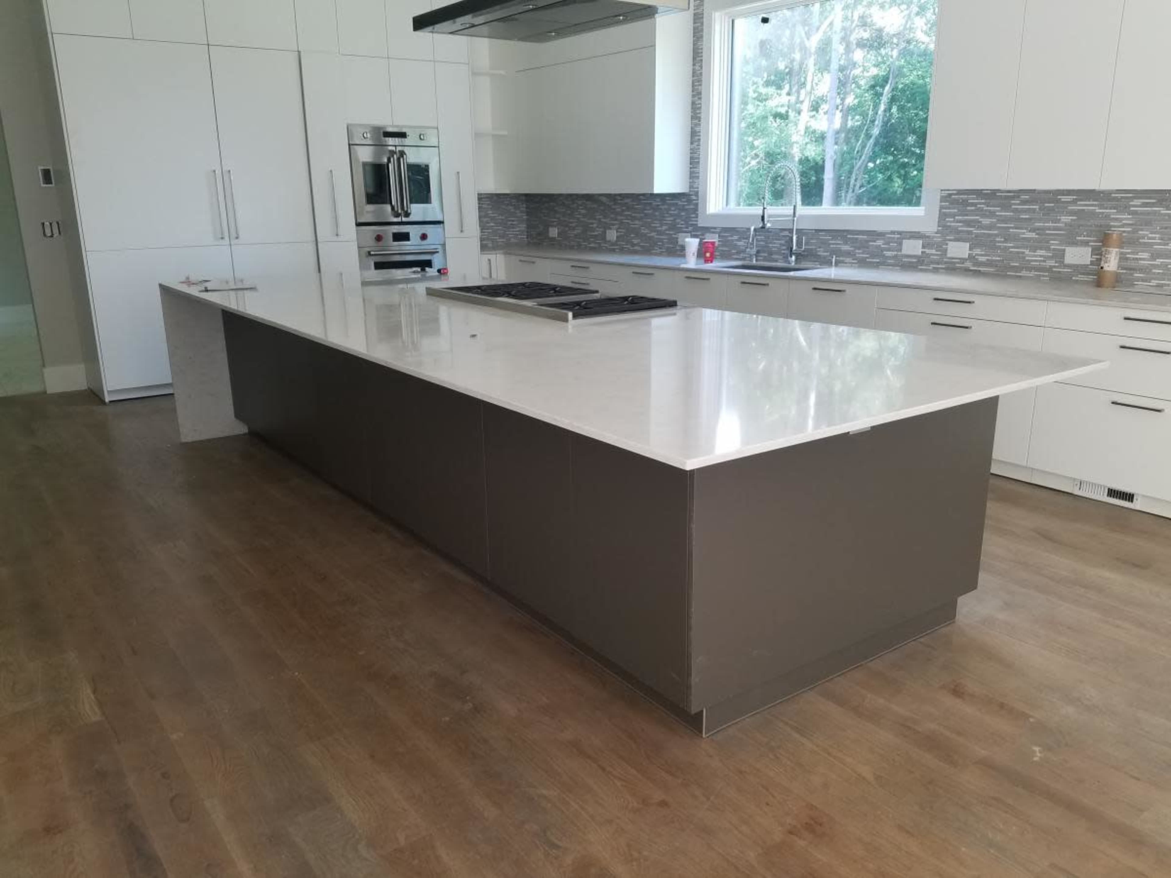A modern kitchen with a large central island featuring a smooth countertop, surrounded by sleek cabinetry and appliances.