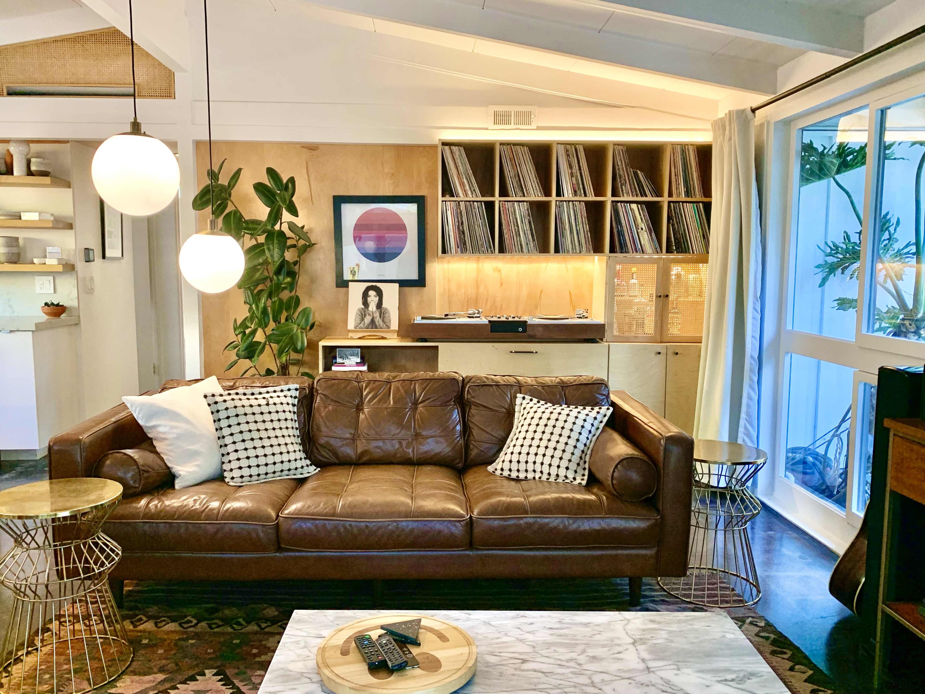 A modern living room featuring a brown leather couch with decorative pillows, a marble coffee table, and a vinyl record display against a wooden wall.