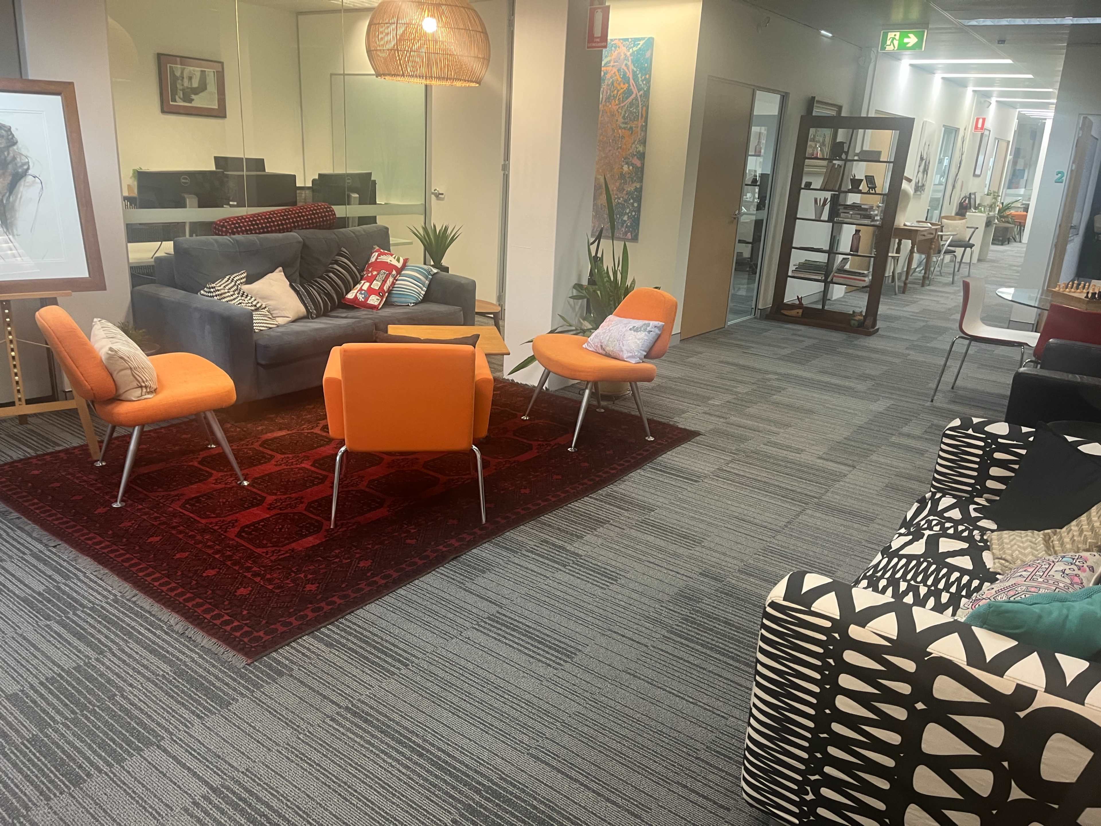 The image shows a modern office interior with colorful seating areas, a patterned sofa, and various decorative elements in a well-lit space.