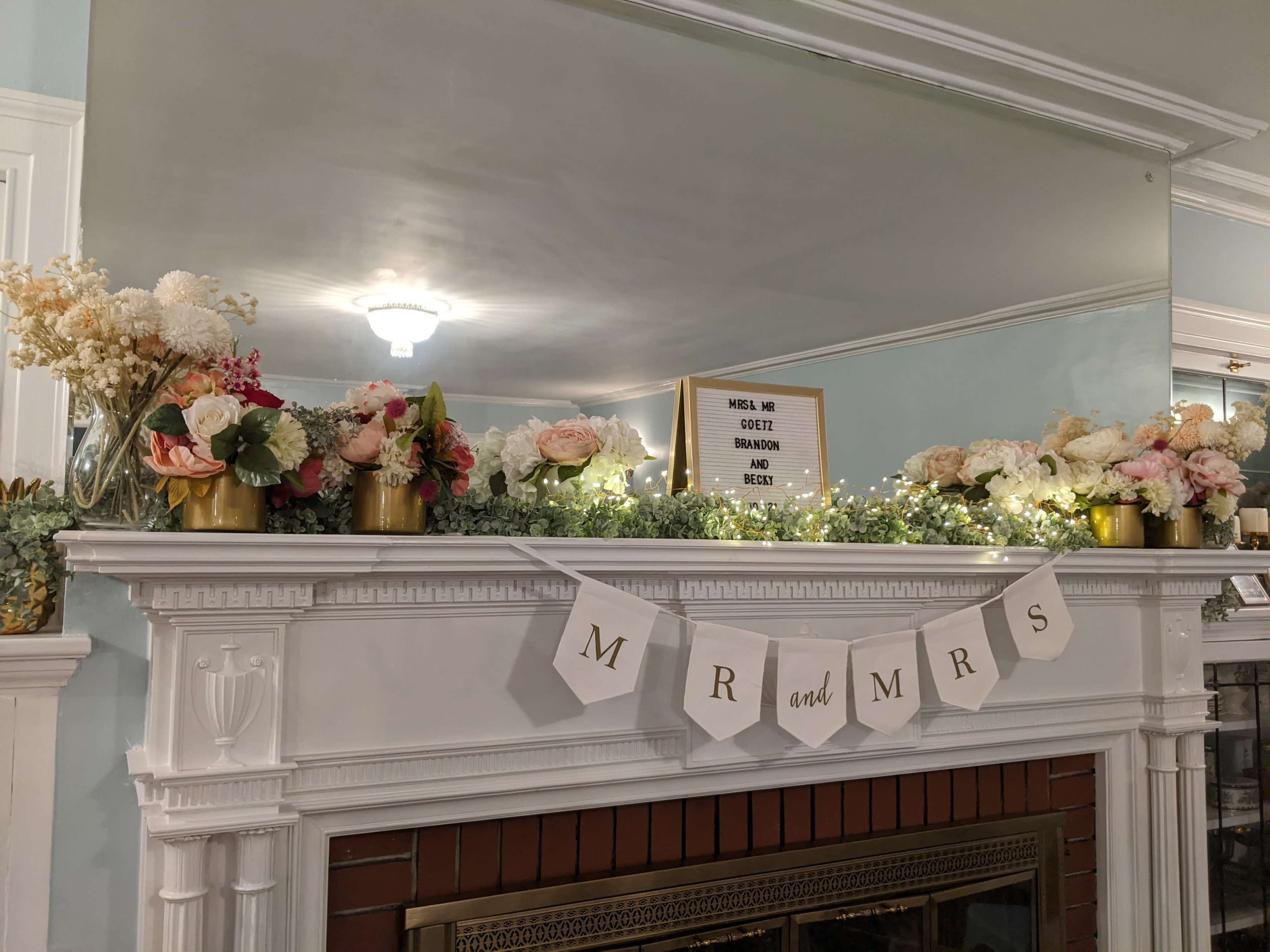 A decorated mantel features a floral arrangement, a sign, and a banner that reads "MR and MRS."