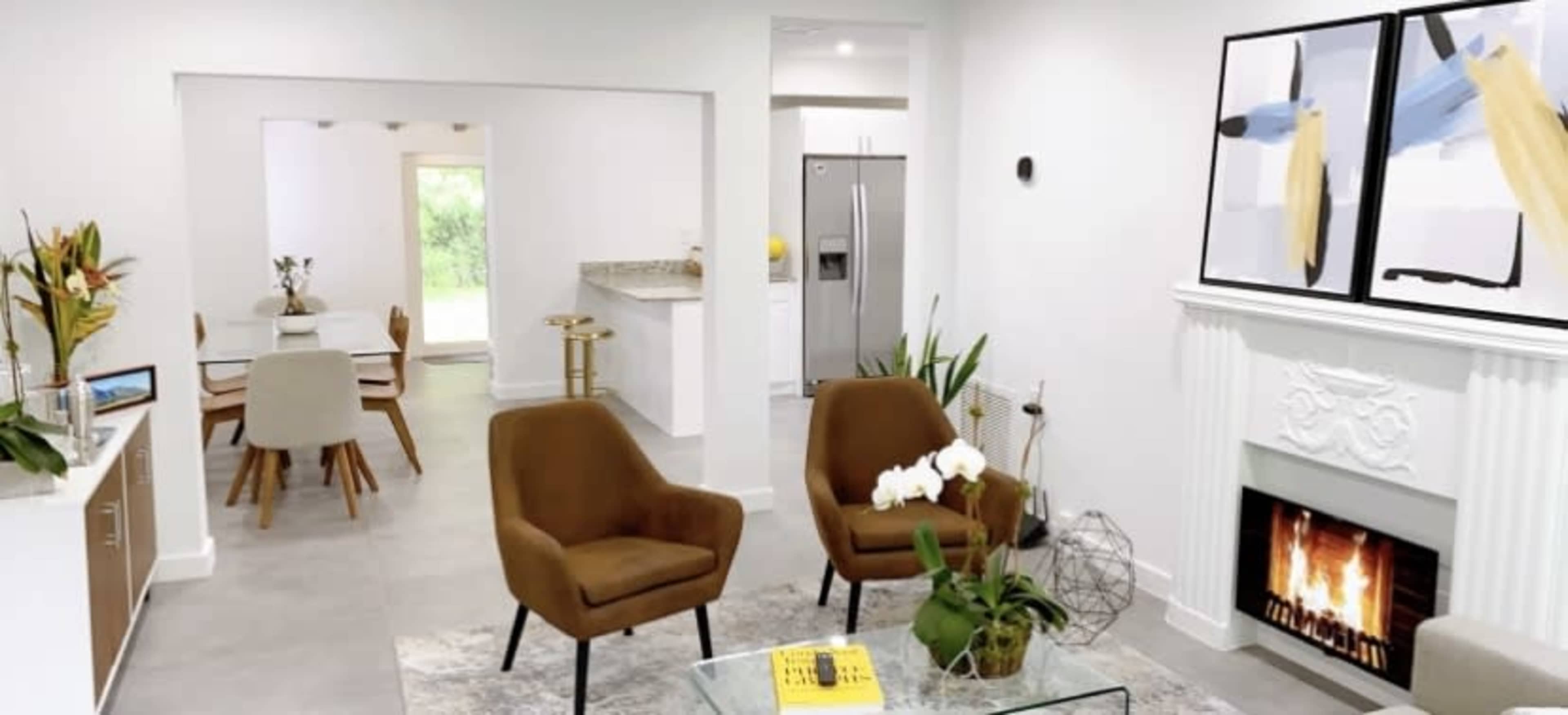 A modern living room with two brown chairs, a glass coffee table, a fireplace, and a view of an adjacent dining area.