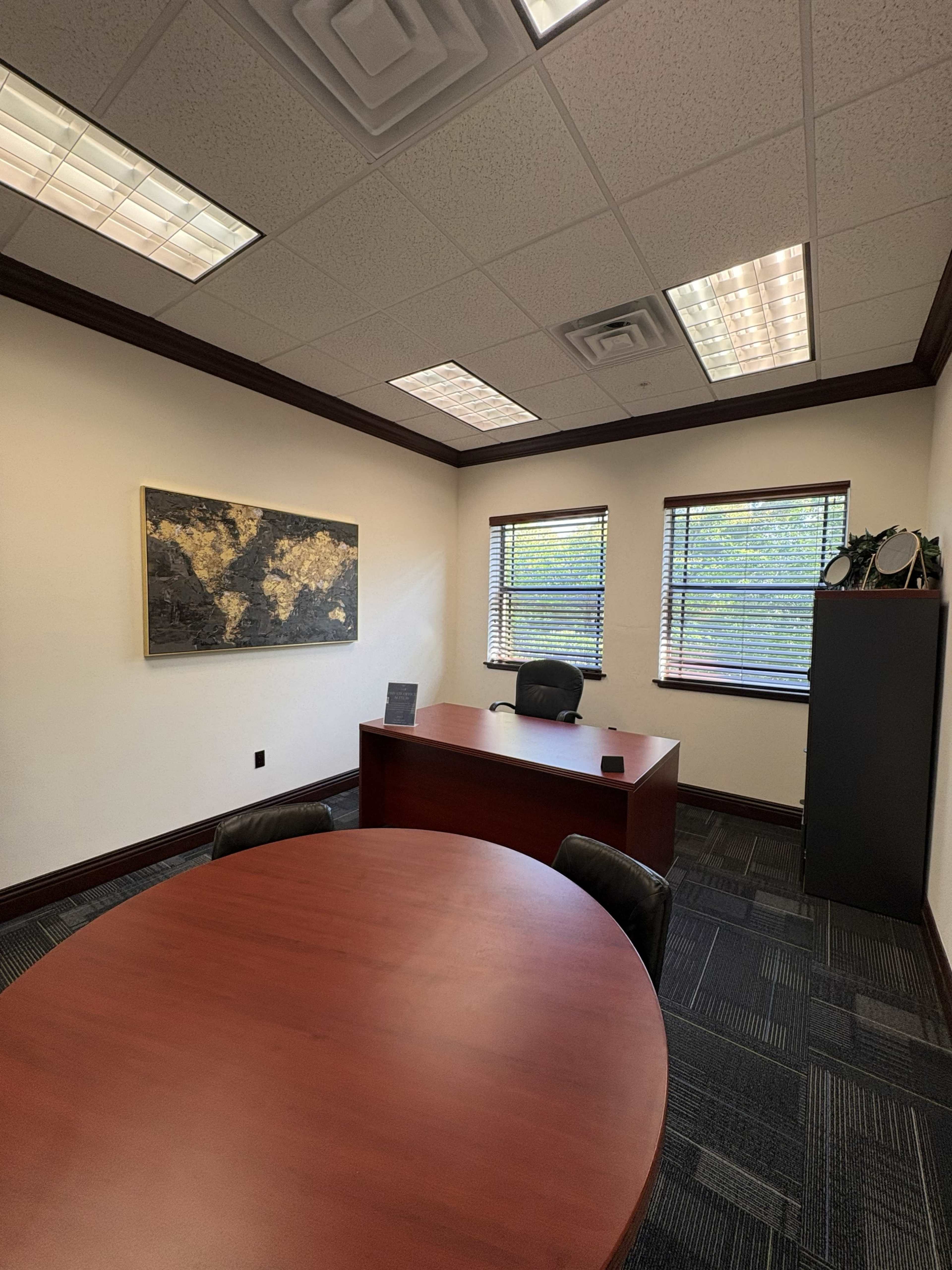 The image shows a modern office with a round conference table, a desk, and a wall map, illuminated by ceiling lights.
