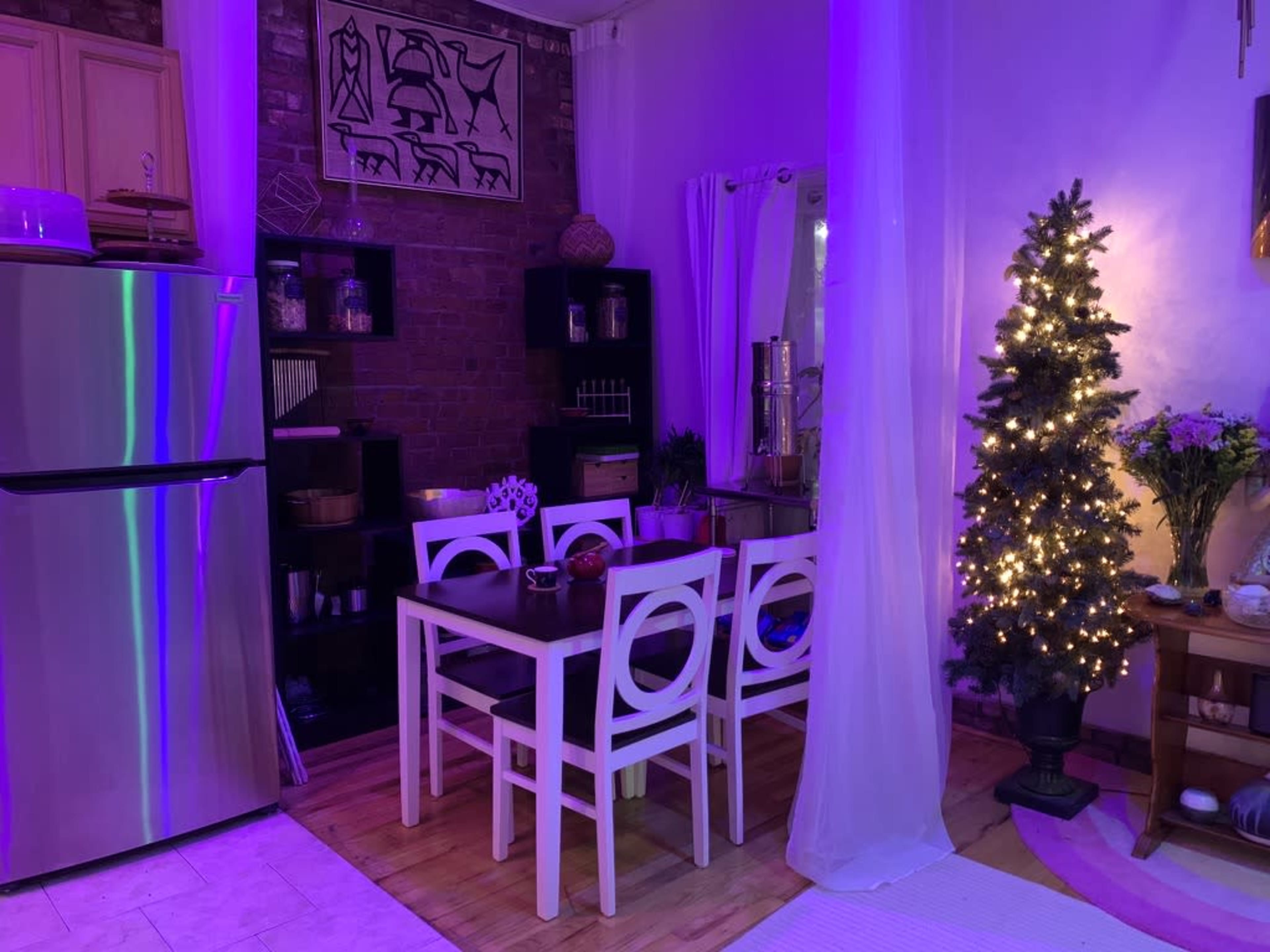 A cozy dining area features a table and chairs, a small decorated Christmas tree, and purple ambient lighting.
