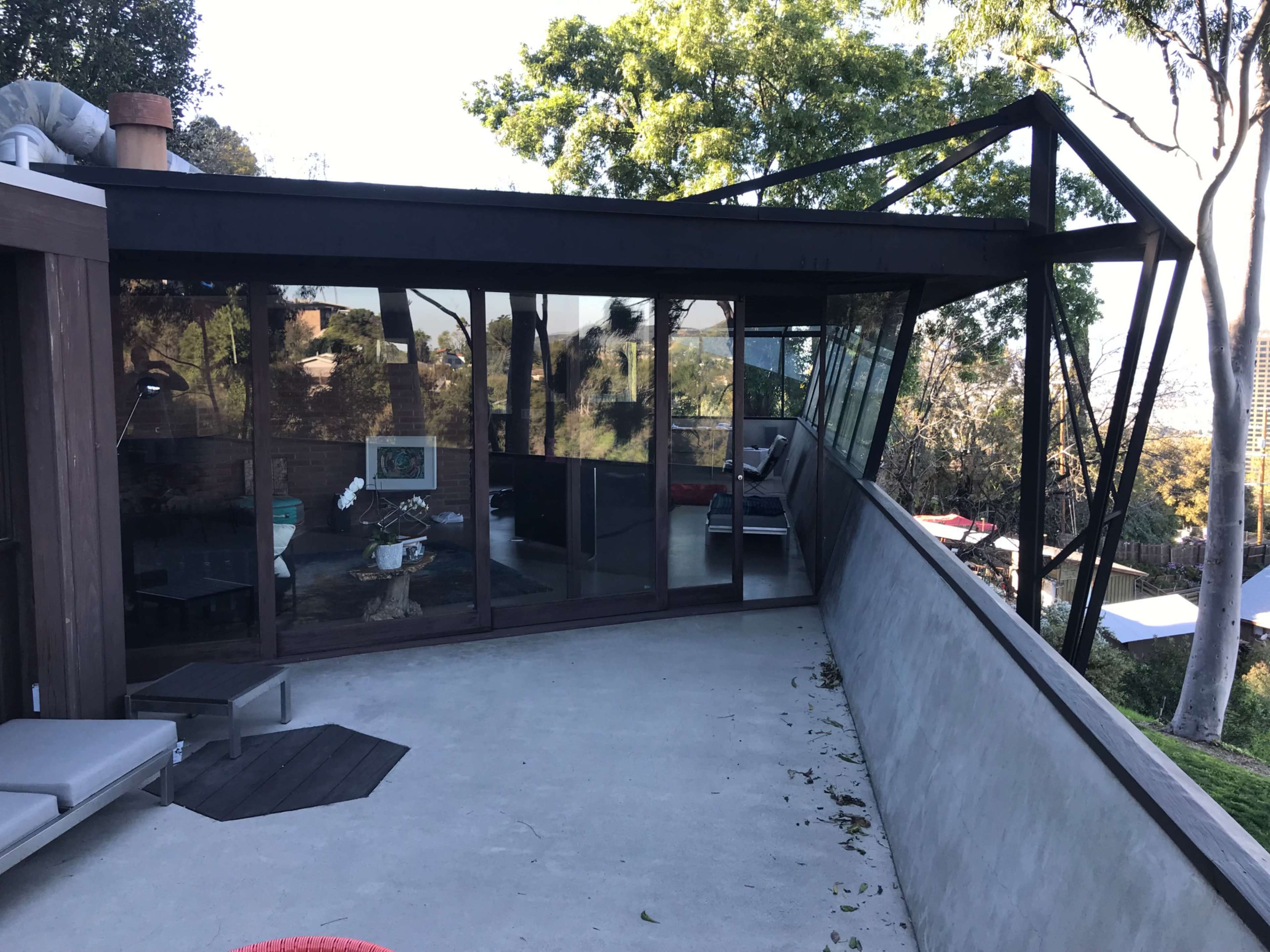 A modern house with a large glass facade and an angular black roof, surrounded by trees.