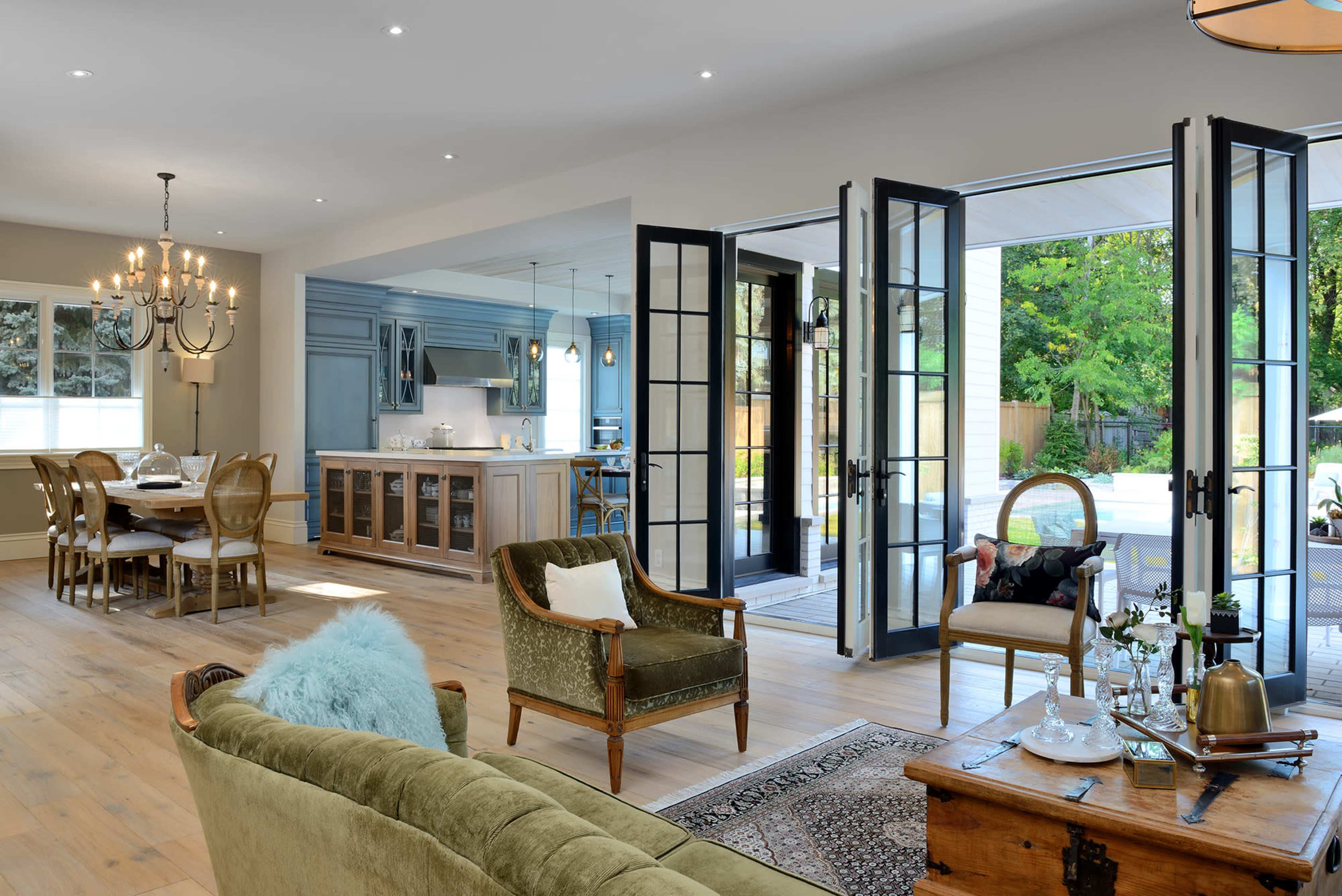 A bright, open living space features a dining area with a chandelier, a kitchen with a modern design, and French doors leading to an outdoor patio.