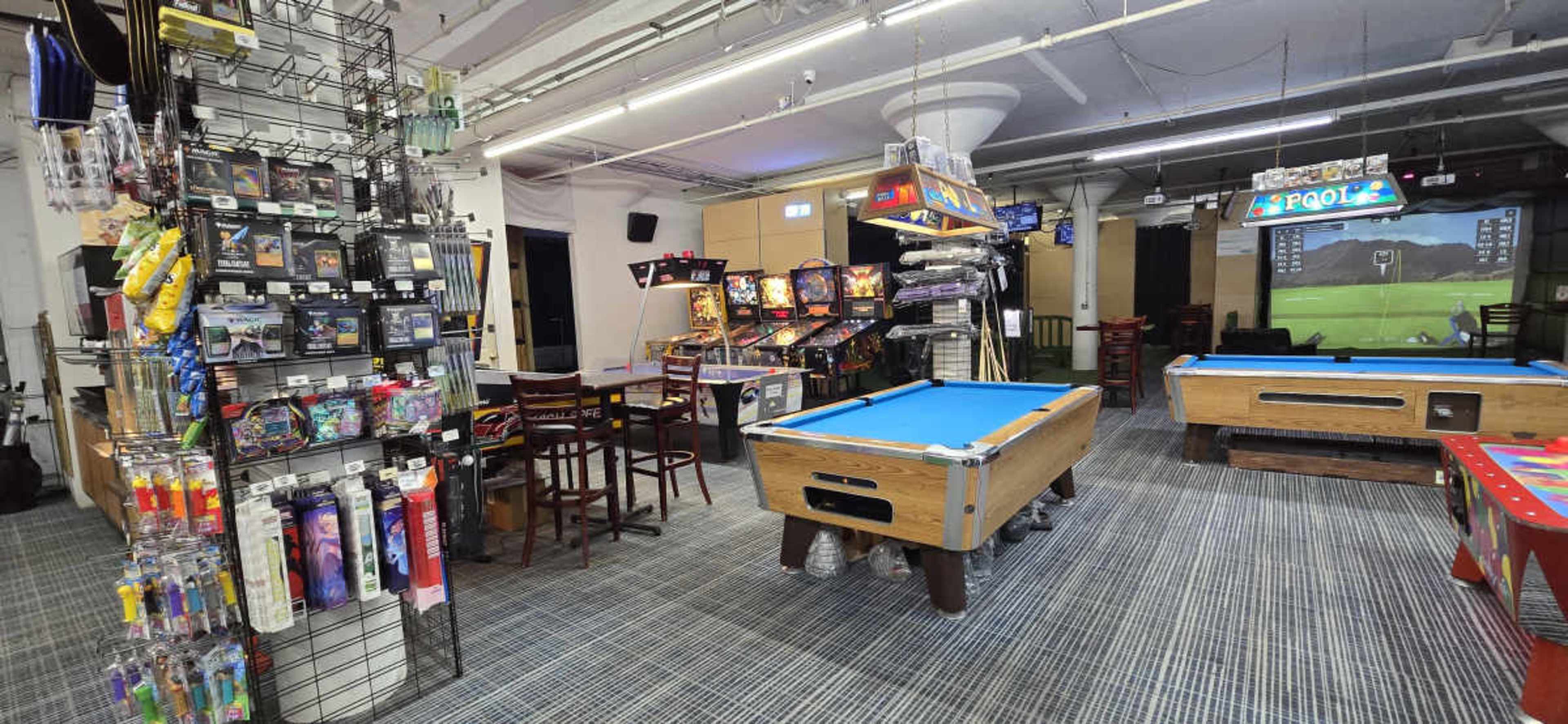 The image shows a gaming entertainment area featuring pool tables, arcade machines, and a corner with colorful merchandise displays.