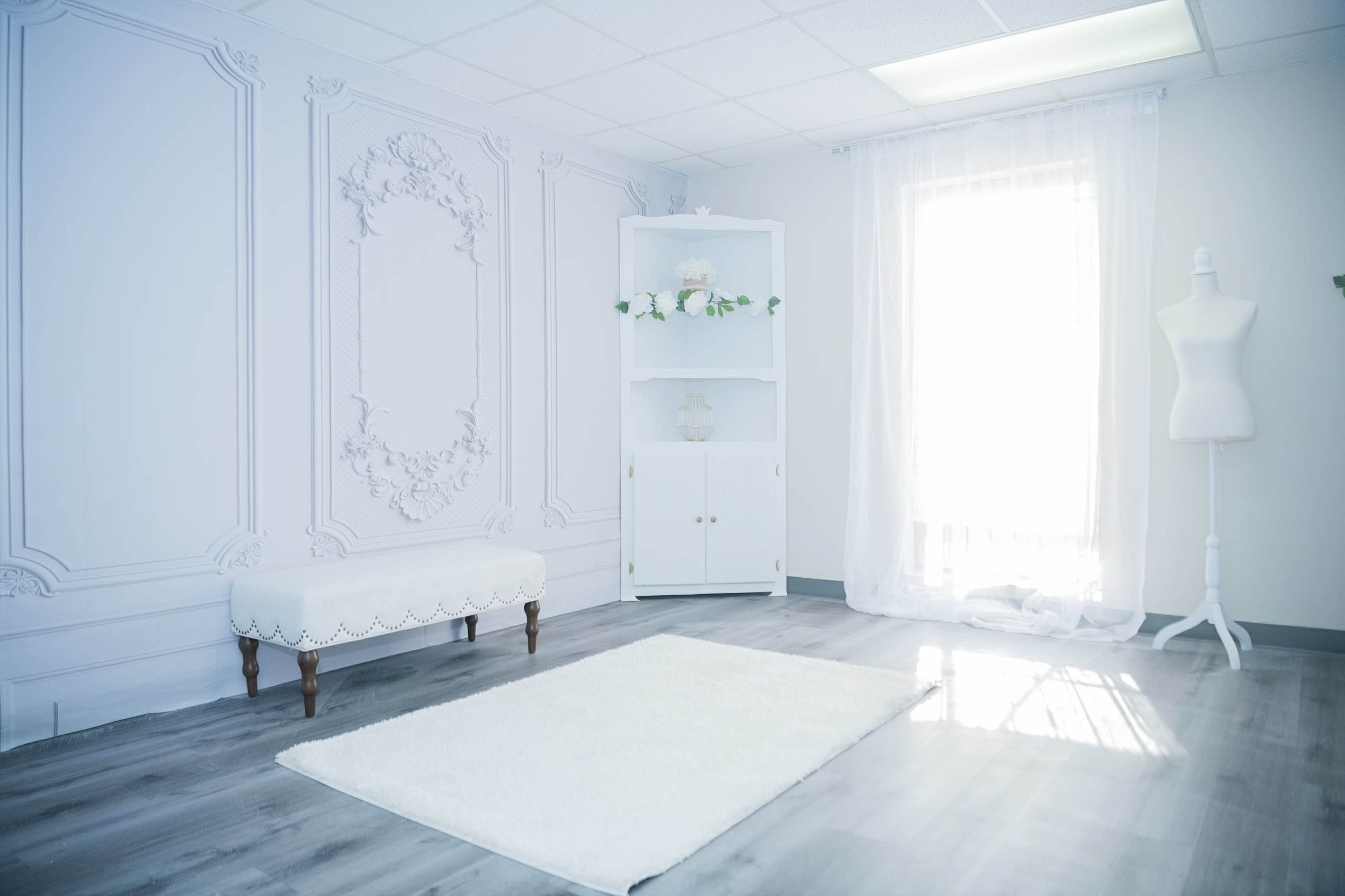 The room features a white wall with ornate molding, a plush bench, and a decorative cabinet, illuminated by natural light from a window.
