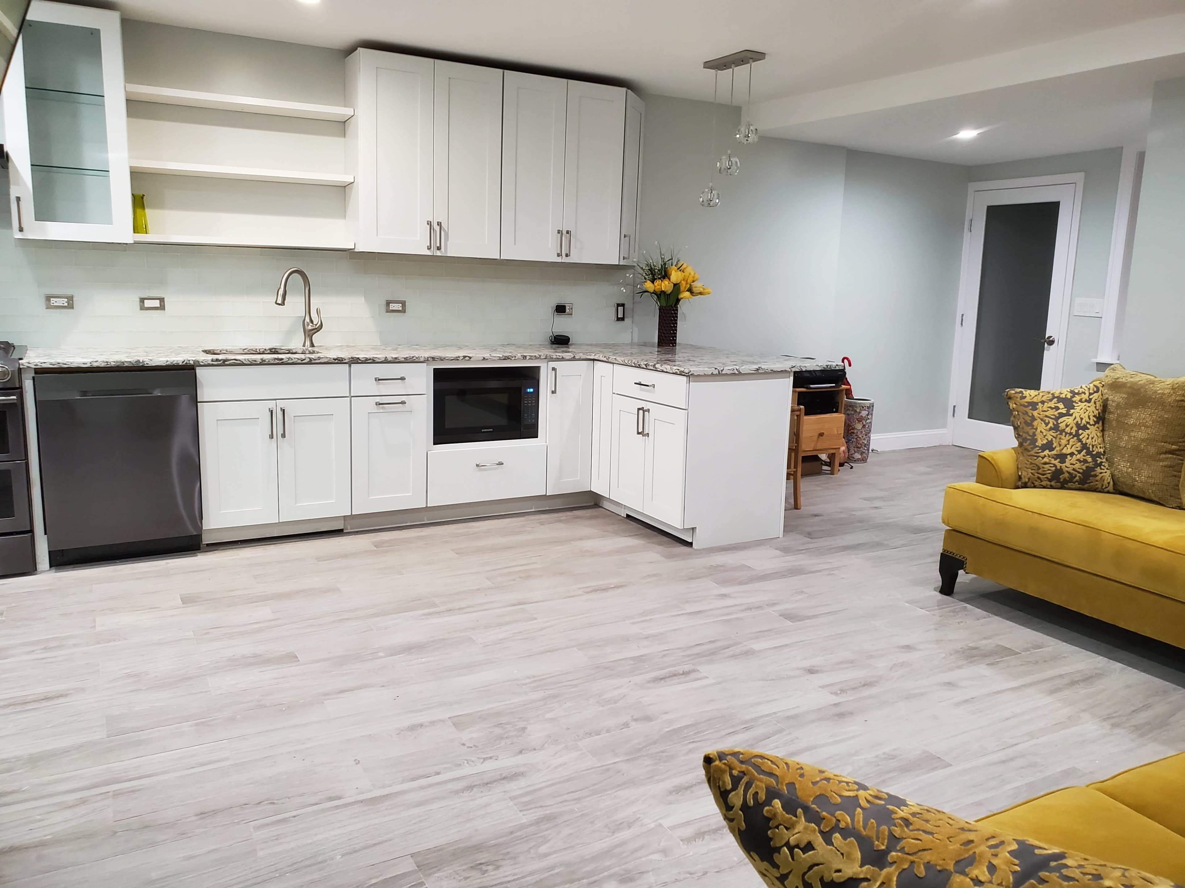 A modern kitchen with white cabinets, granite countertops, and a yellow sofa in the living area.