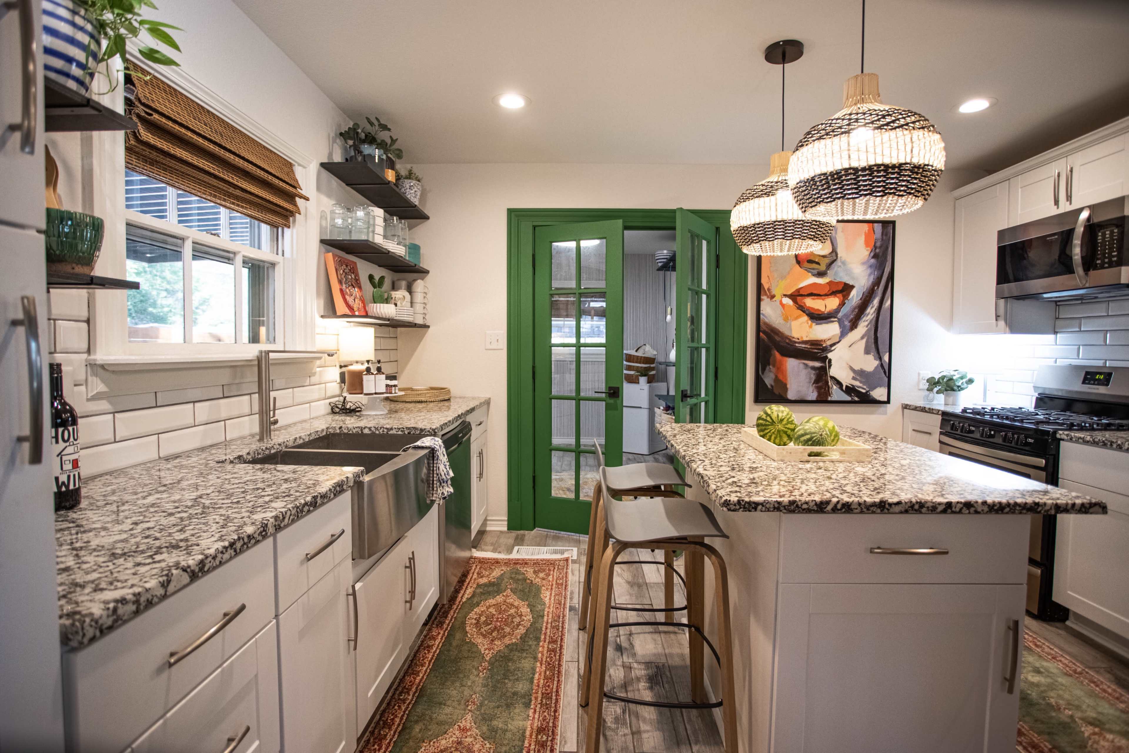 A modern kitchen features a granite countertop island, natural wood accents, and green French doors leading to an outdoor space.