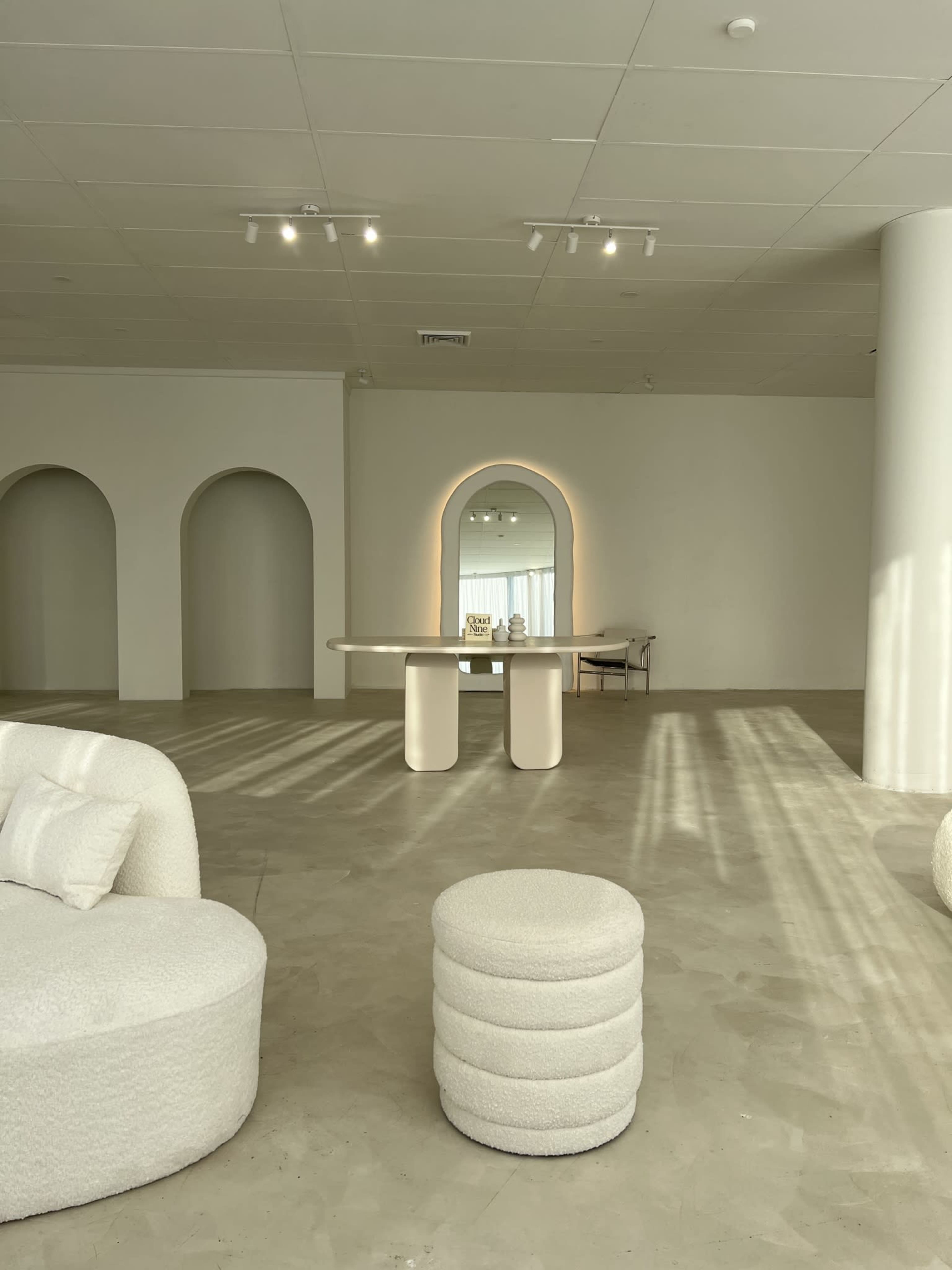 A minimalist interior space with curved arches, a central table, and a mirror reflecting light.