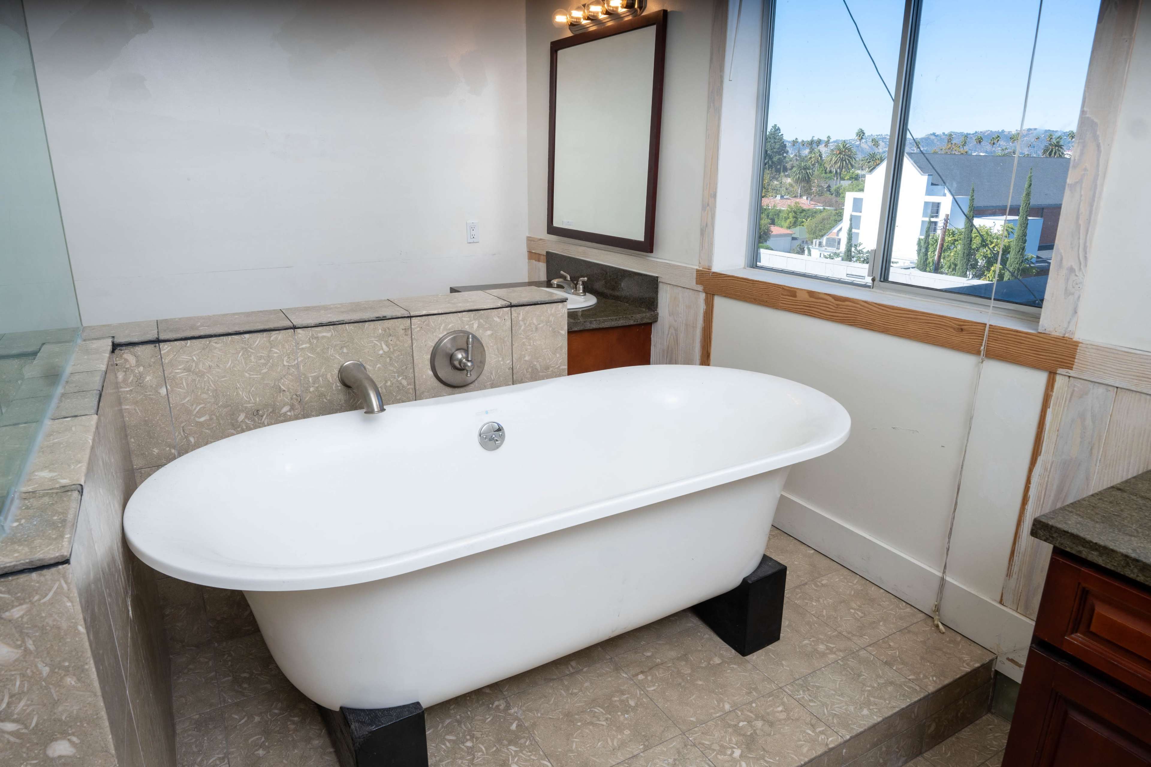 A spacious bathroom featuring a freestanding white bathtub, a large mirror, and a window with a view.
