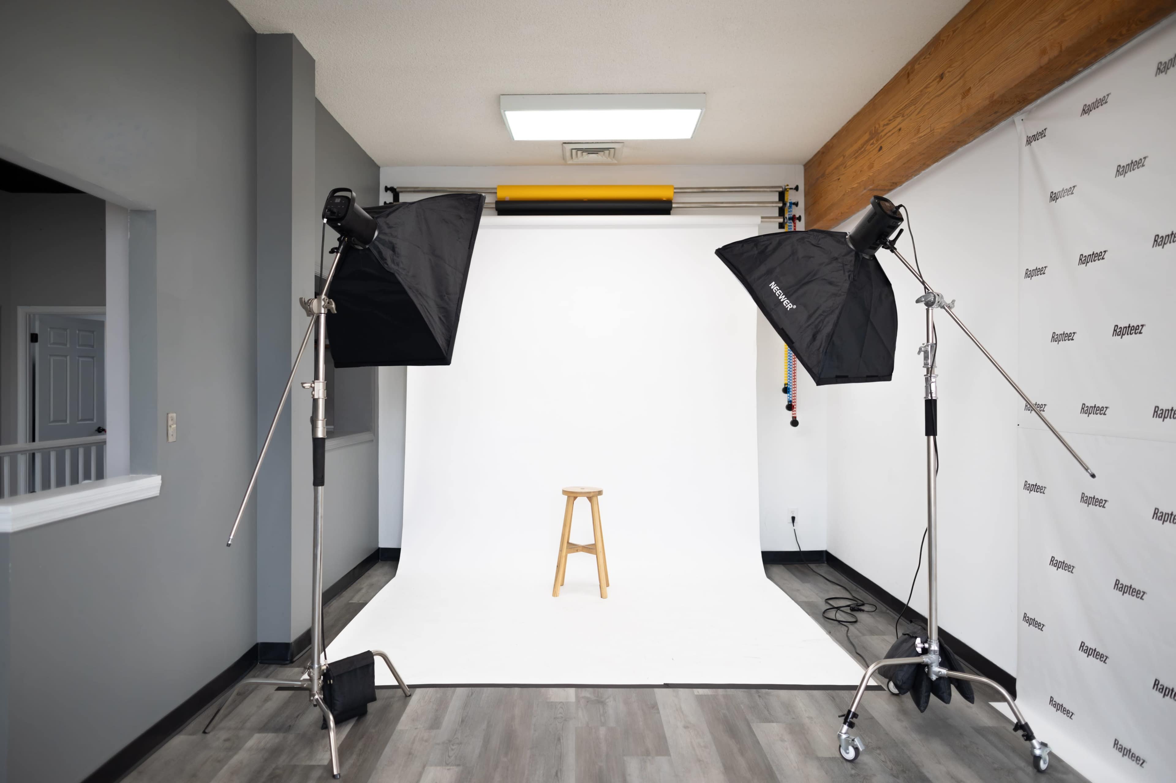 The image shows a photography studio setup with two softbox lights positioned on either side of a wooden stool in front of a white backdrop.
