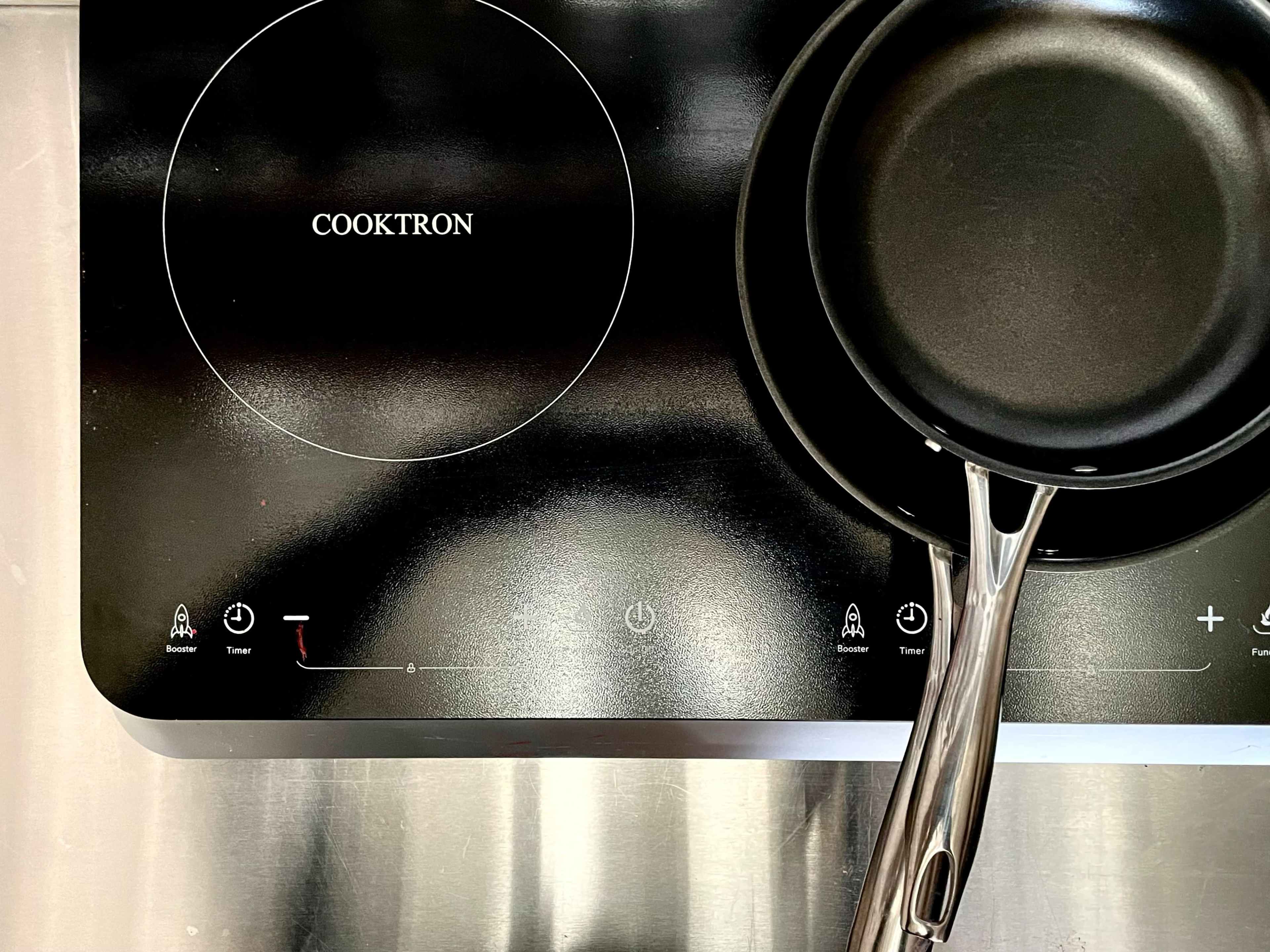A black cooktop with the brand "COOKTRON" and a frying pan placed on it.
