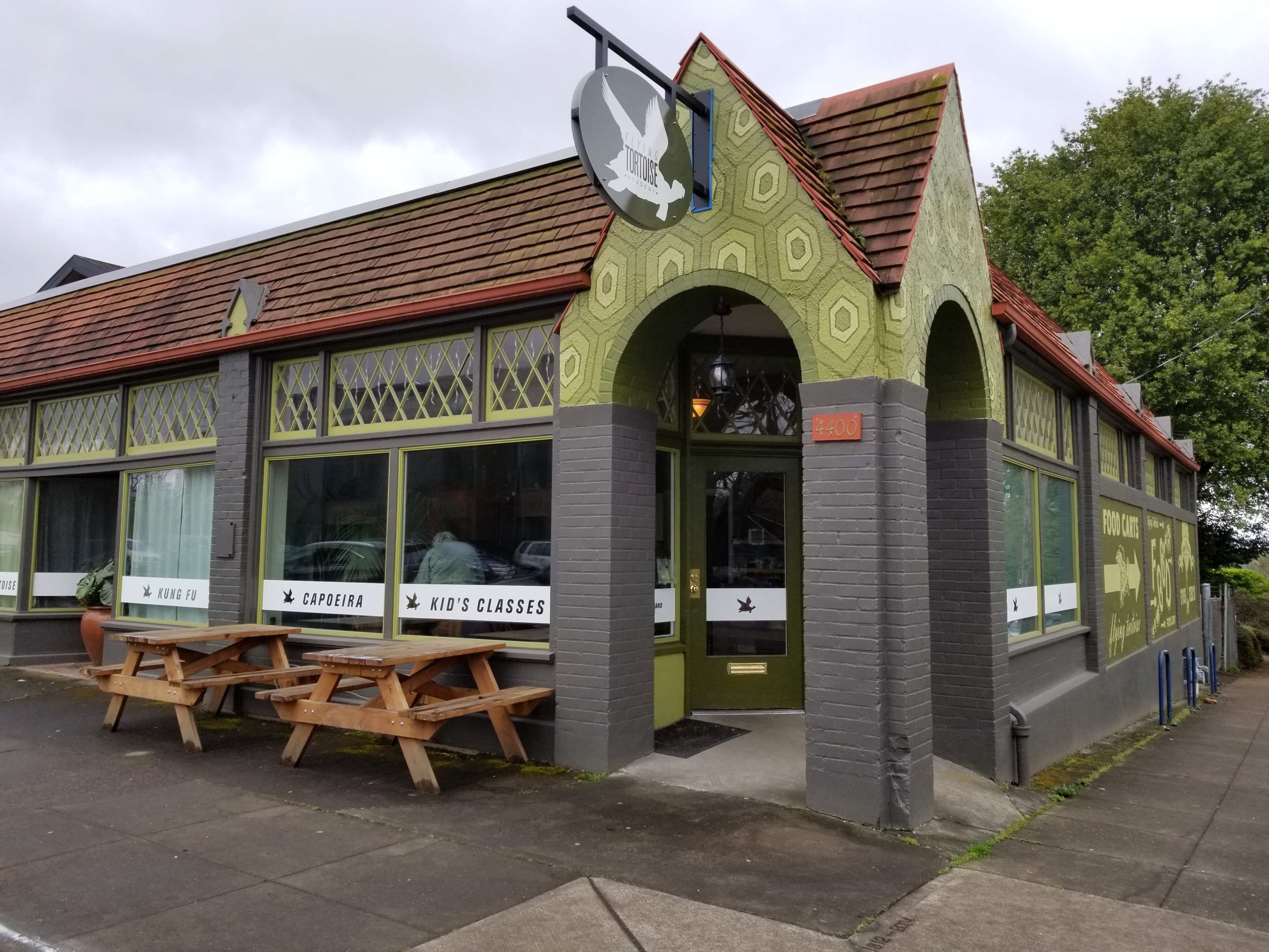 A green and gray restaurant building with large windows and outdoor seating, located at 2400 on the street.