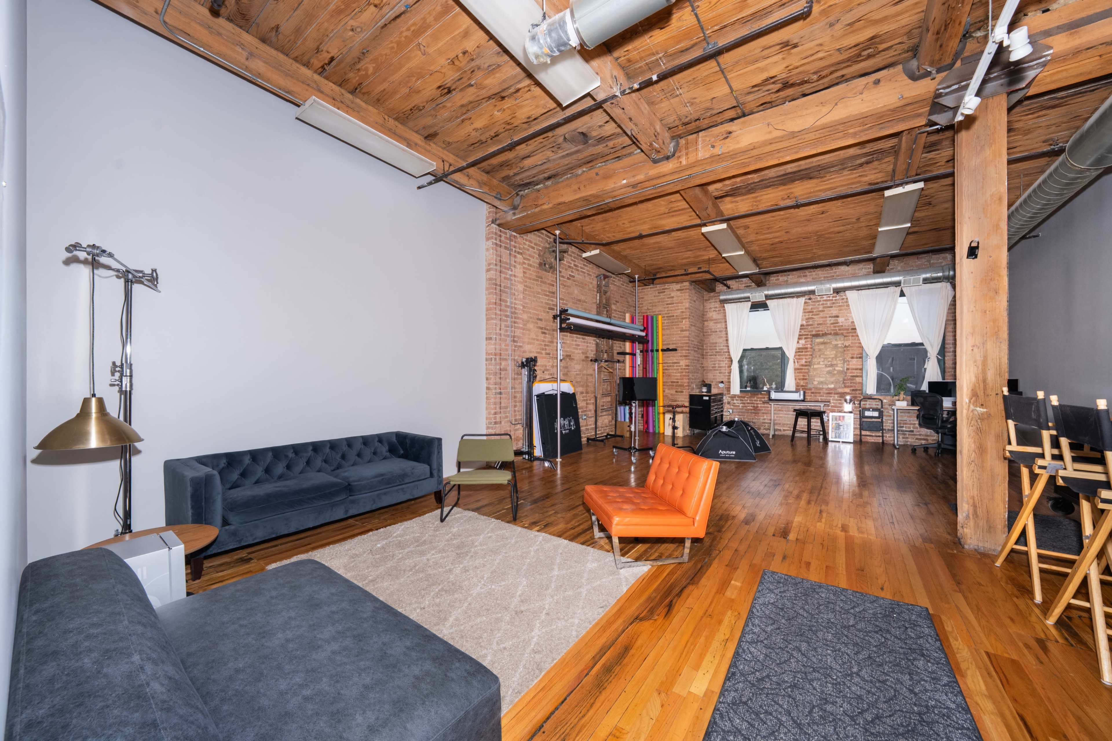 The image shows a spacious loft with hardwood floors, exposed brick walls, and a mix of modern furniture, including a blue sofa and an orange chair.
