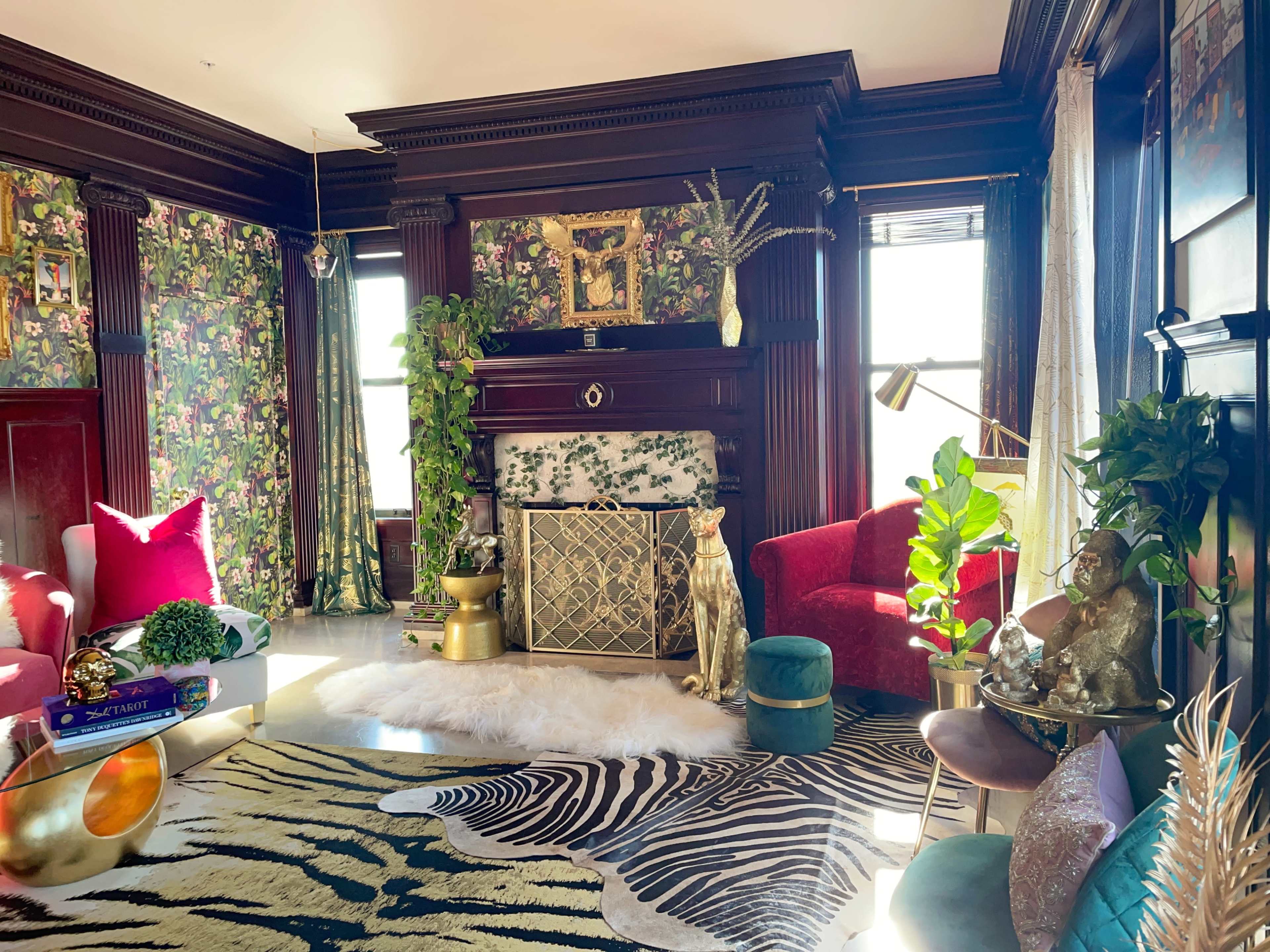 The living room features a floral wallpaper, a green fireplace, and a zebra-patterned rug surrounded by various decorative plants and furniture.