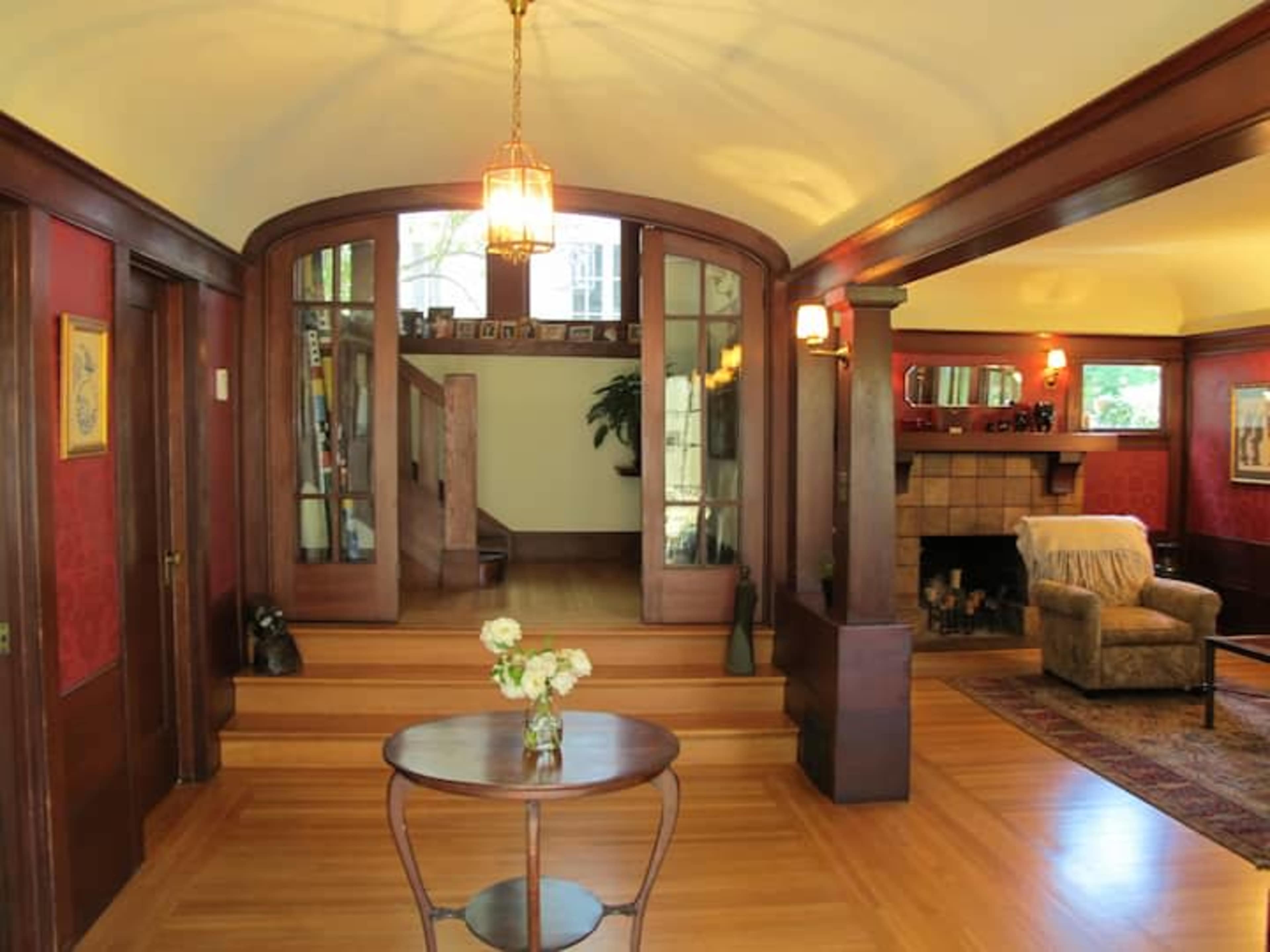 An entrance hallway leading to a living area with a small table and a fireplace, framed by wooden architecture and red walls.