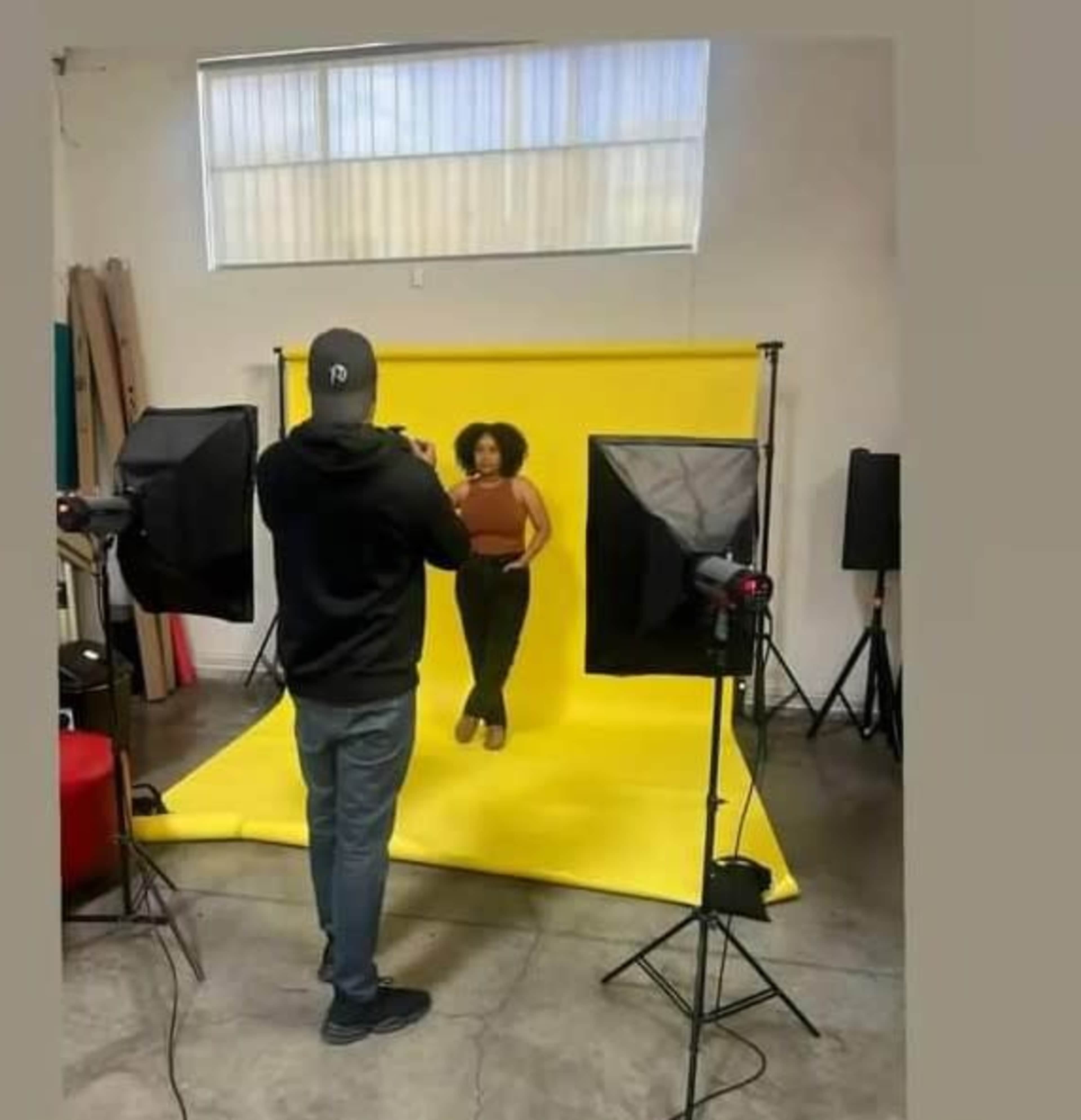 A photographer captures a model posing against a bright yellow backdrop in a studio setting.