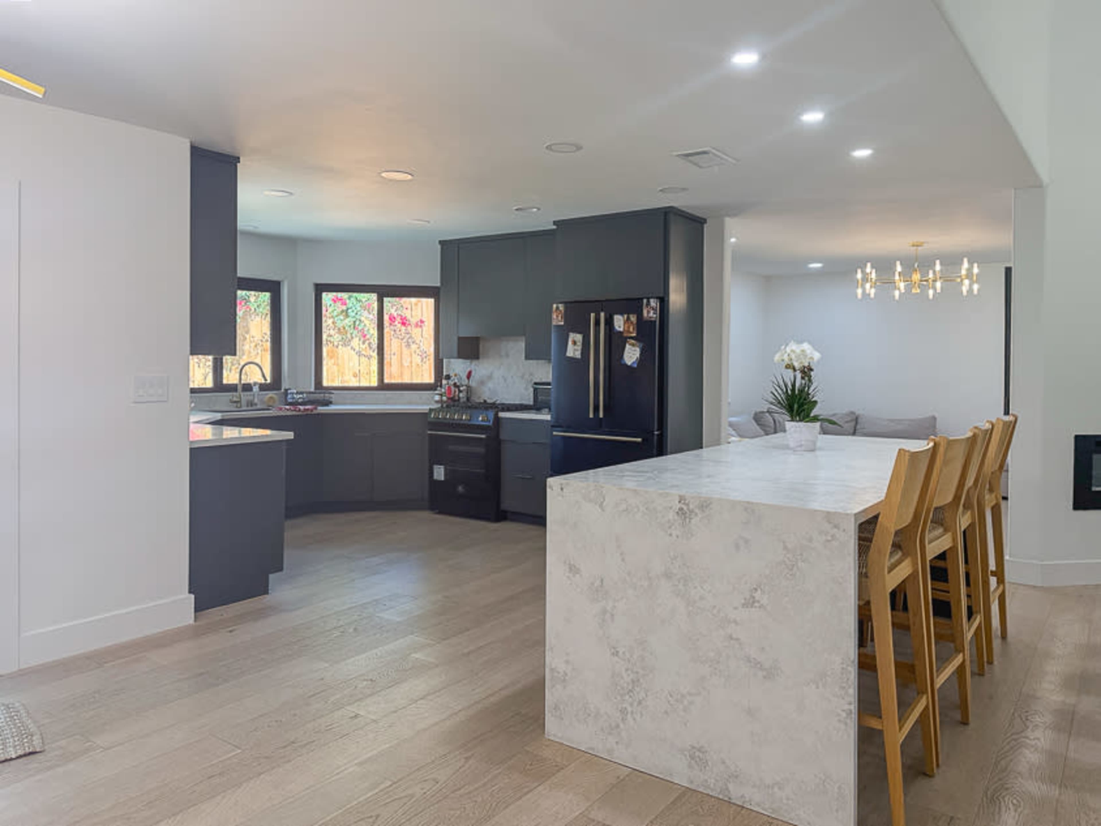 The image shows a modern kitchen with dark cabinets, a large white island with seating, and a dining area featuring a light fixture.