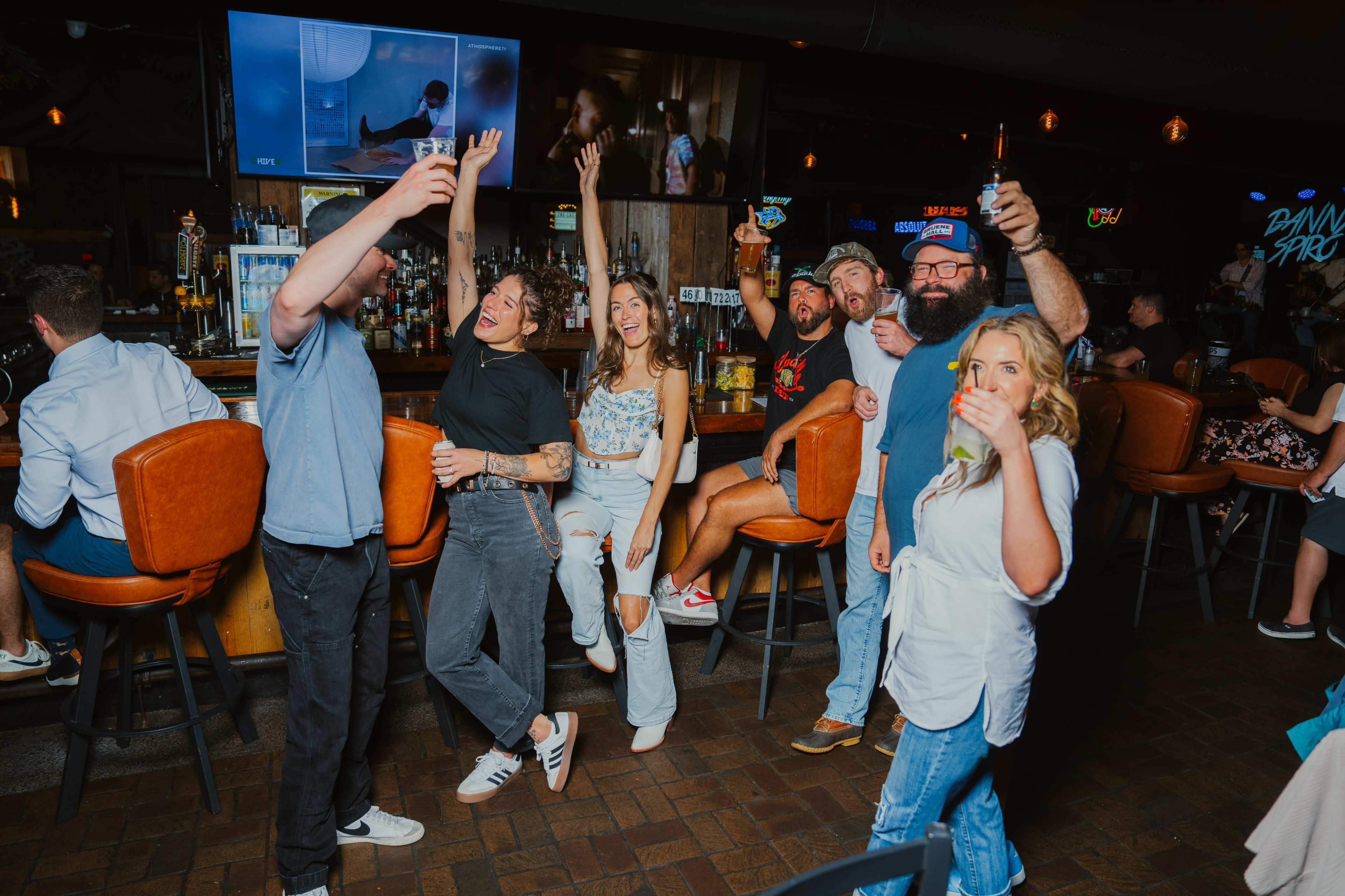 A group of people is celebrating at a lively bar, posing together with drinks and smiling.