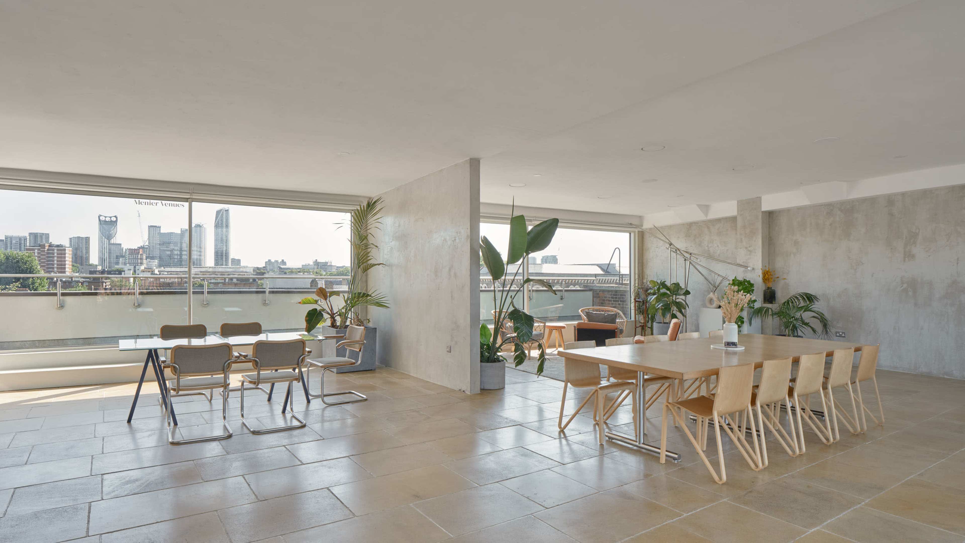 The image depicts a spacious, modern interior with a dining area featuring a large table and chairs, complemented by large windows that offer a view of a city skyline.
