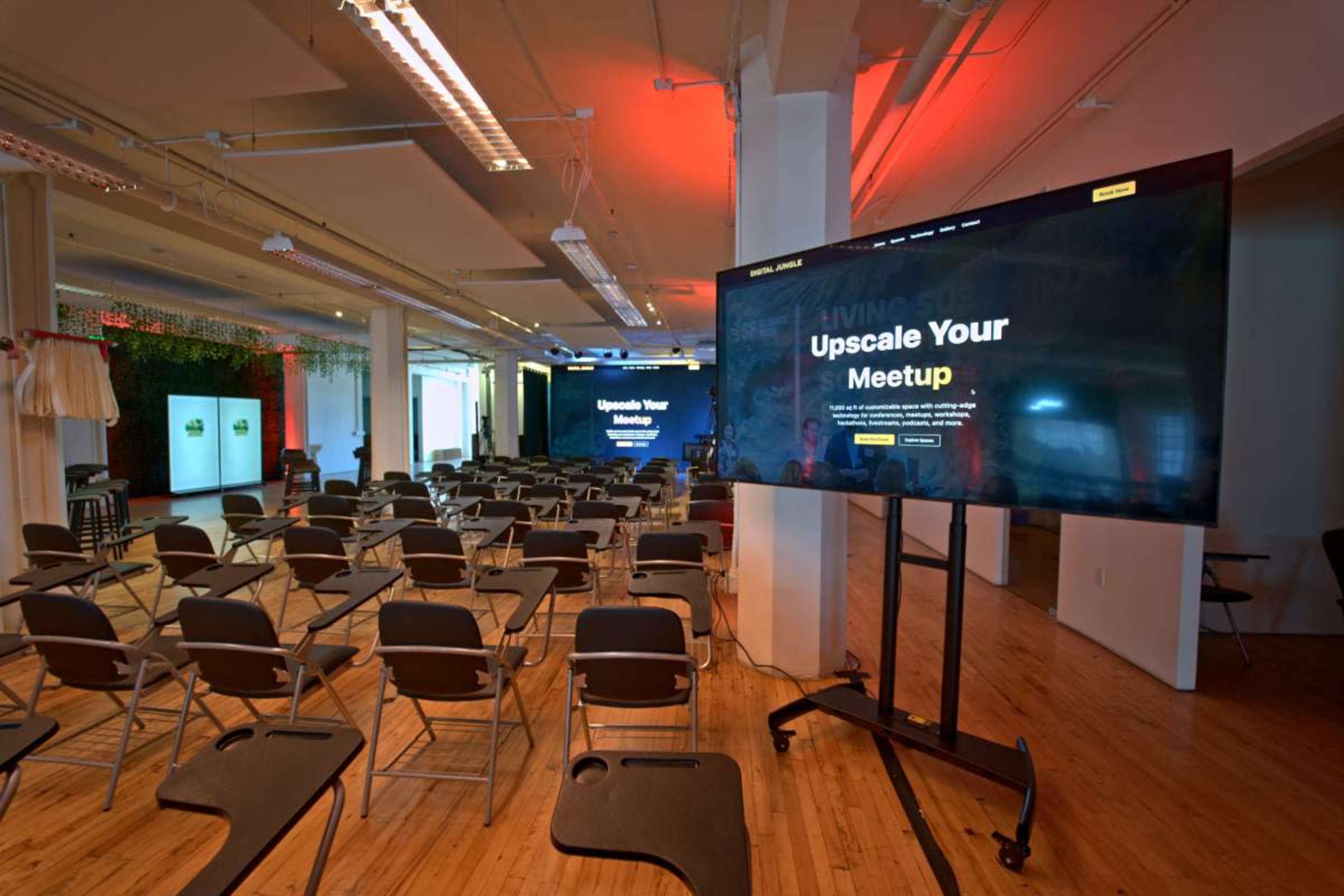 A large screen displaying "Upscale Your Meetup" is positioned in a room filled with rows of empty chairs.