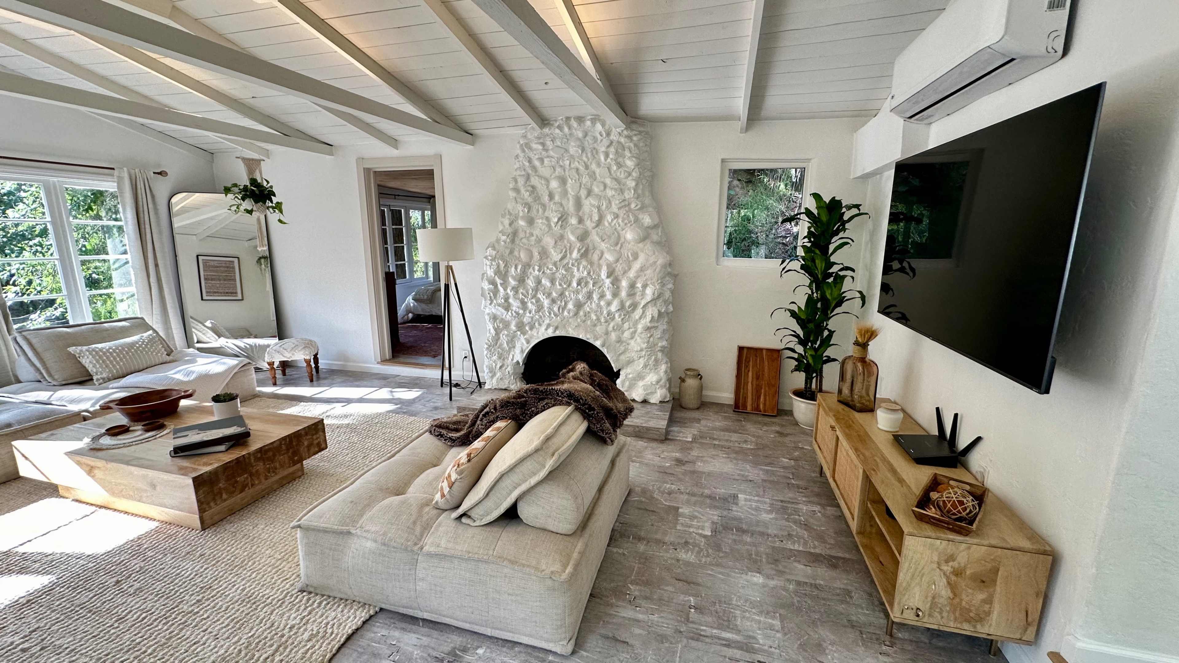 A bright, minimalist living room featuring a white stone fireplace, a large television mounted on the wall, and a cozy seating area with a coffee table.