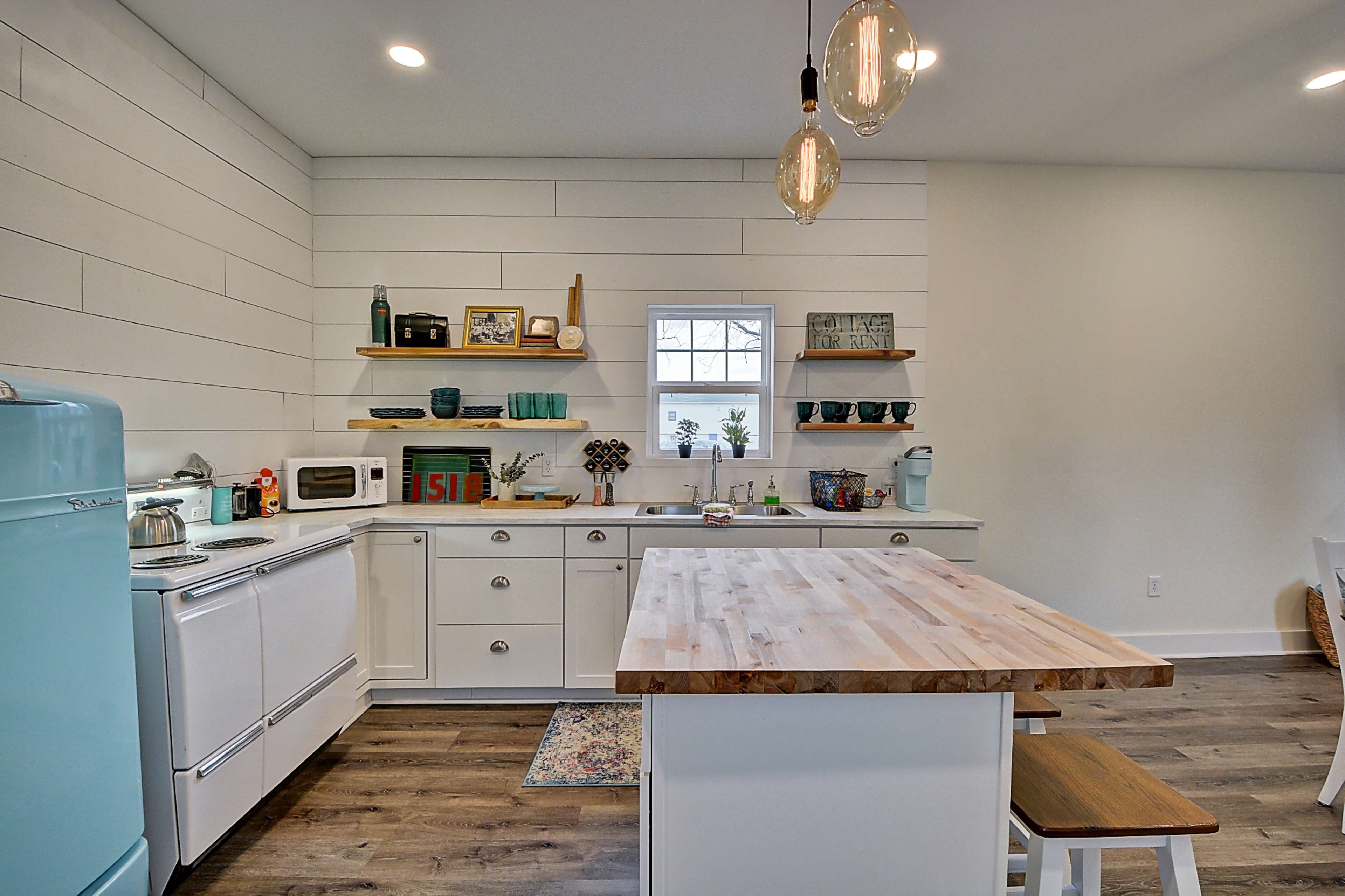 A modern kitchen with white shiplap walls, wooden shelves, a light wood countertop, and mint green accents.