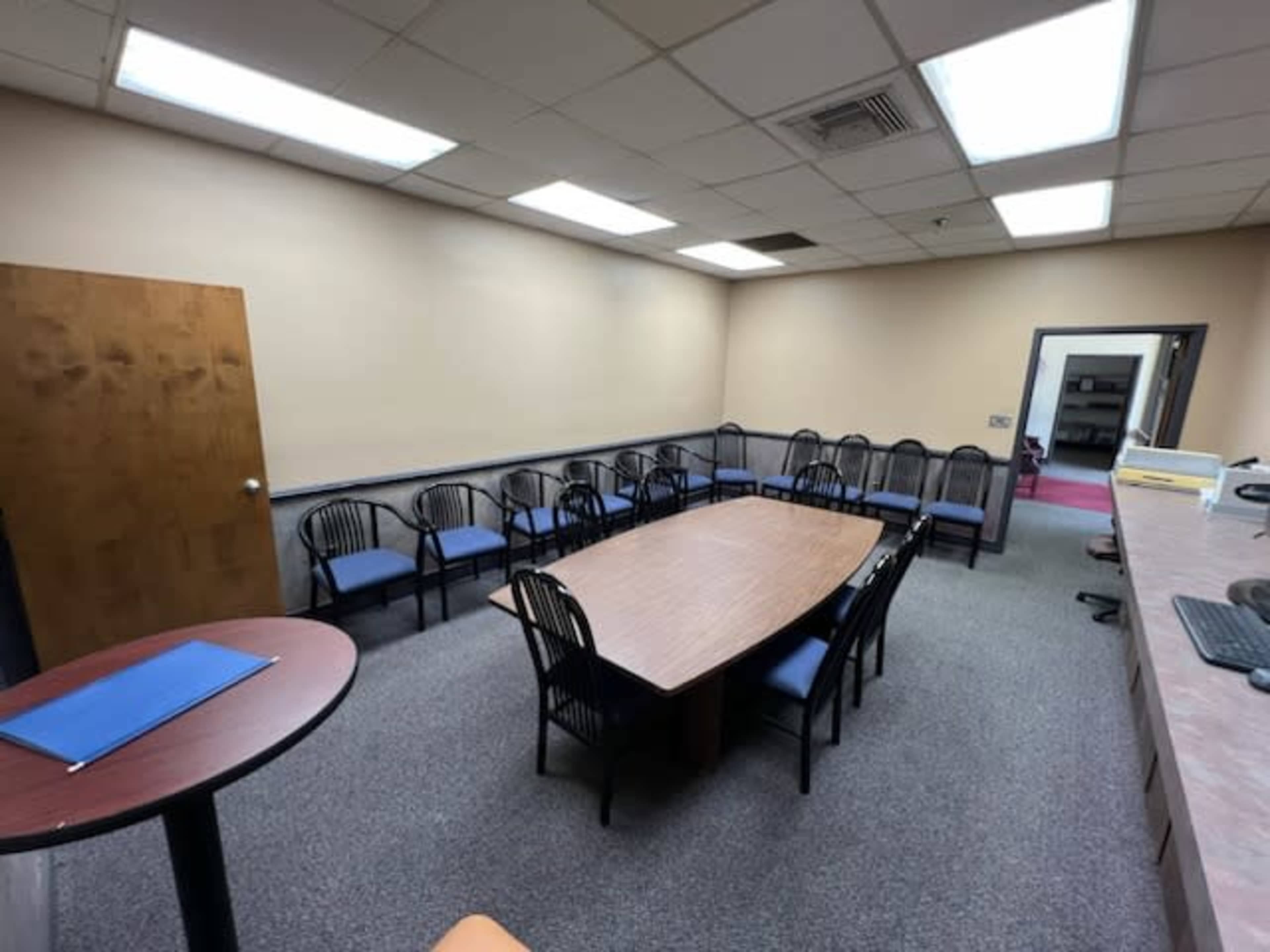A conference room with a large rectangular table surrounded by black chairs, and a small round table in one corner.