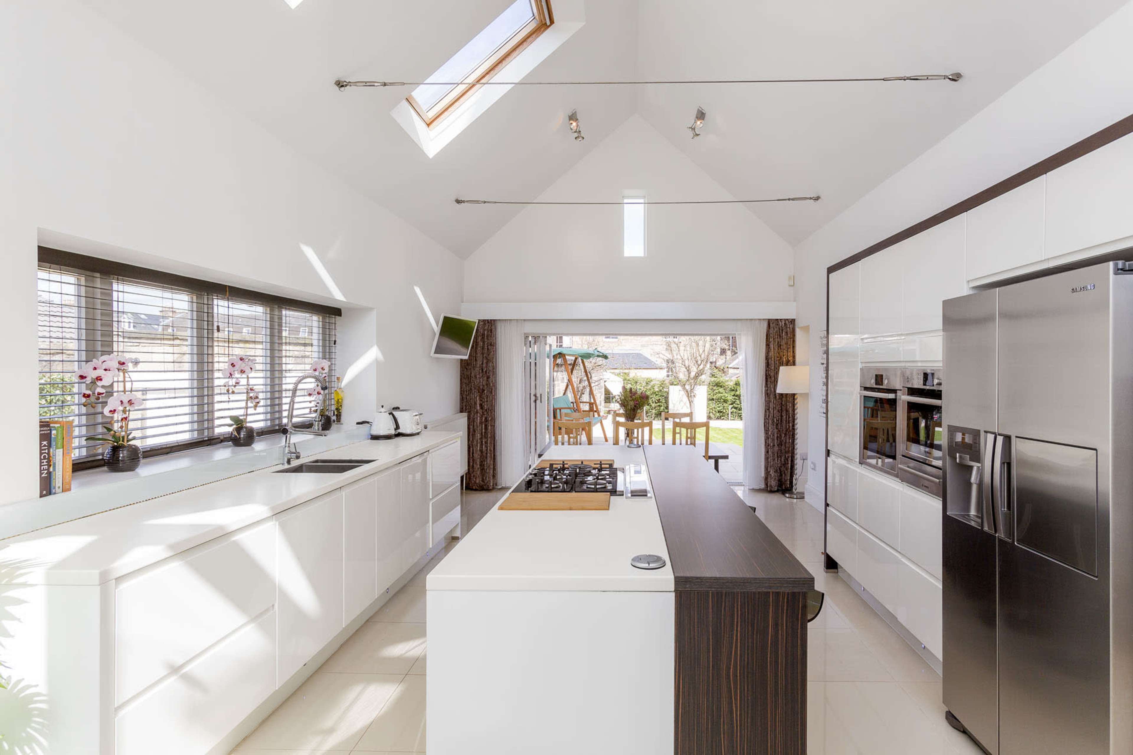 A modern kitchen featuring white cabinetry, a central island with a cooktop, and large windows leading to an outdoor dining area.
