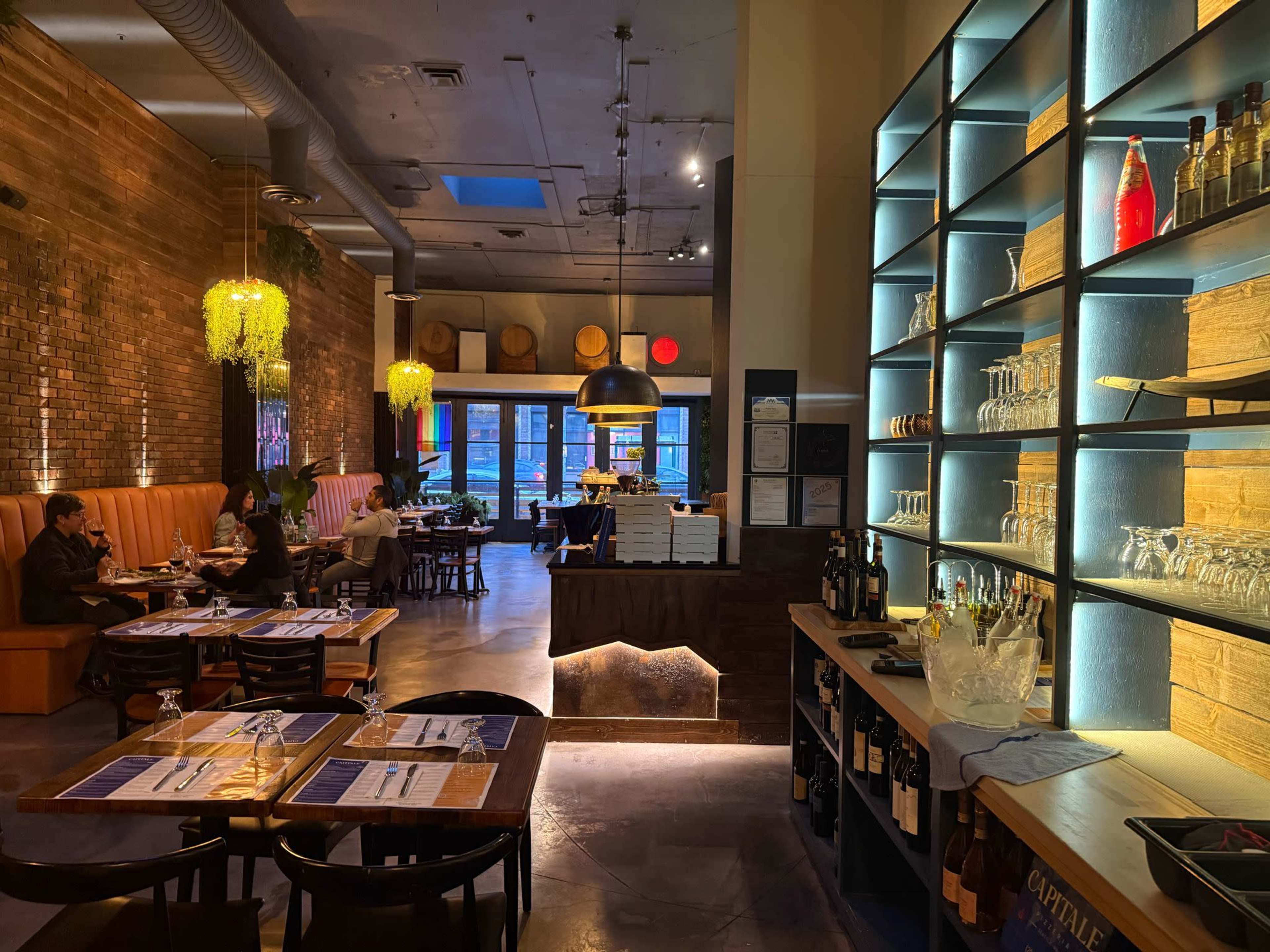 The image depicts a modern restaurant interior with wooden accents, illuminated shelves, and a dining area featuring tables and booths.