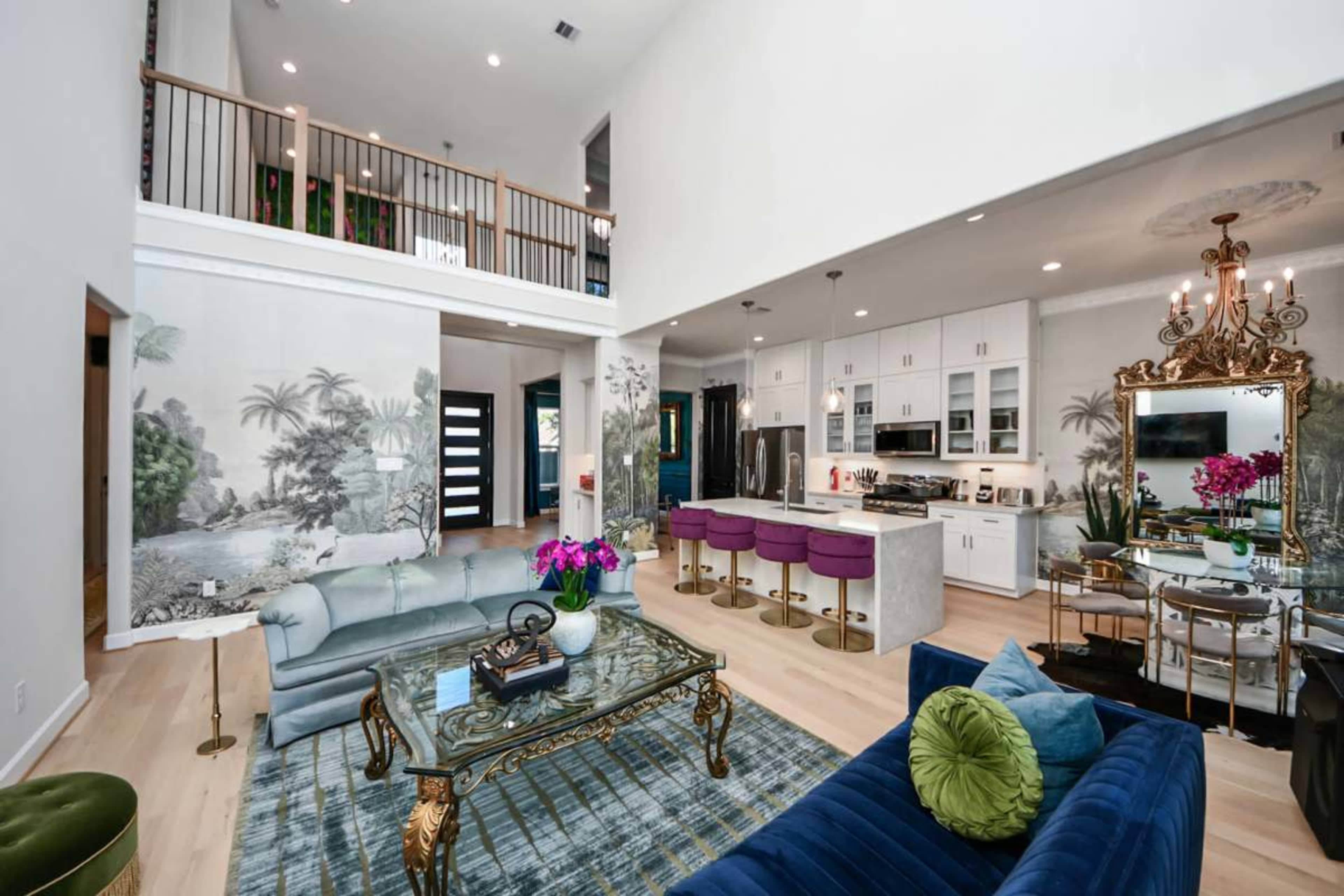 The image shows a spacious living area with a kitchen featuring modern appliances, stylish seating arrangements, and decorative wall art.