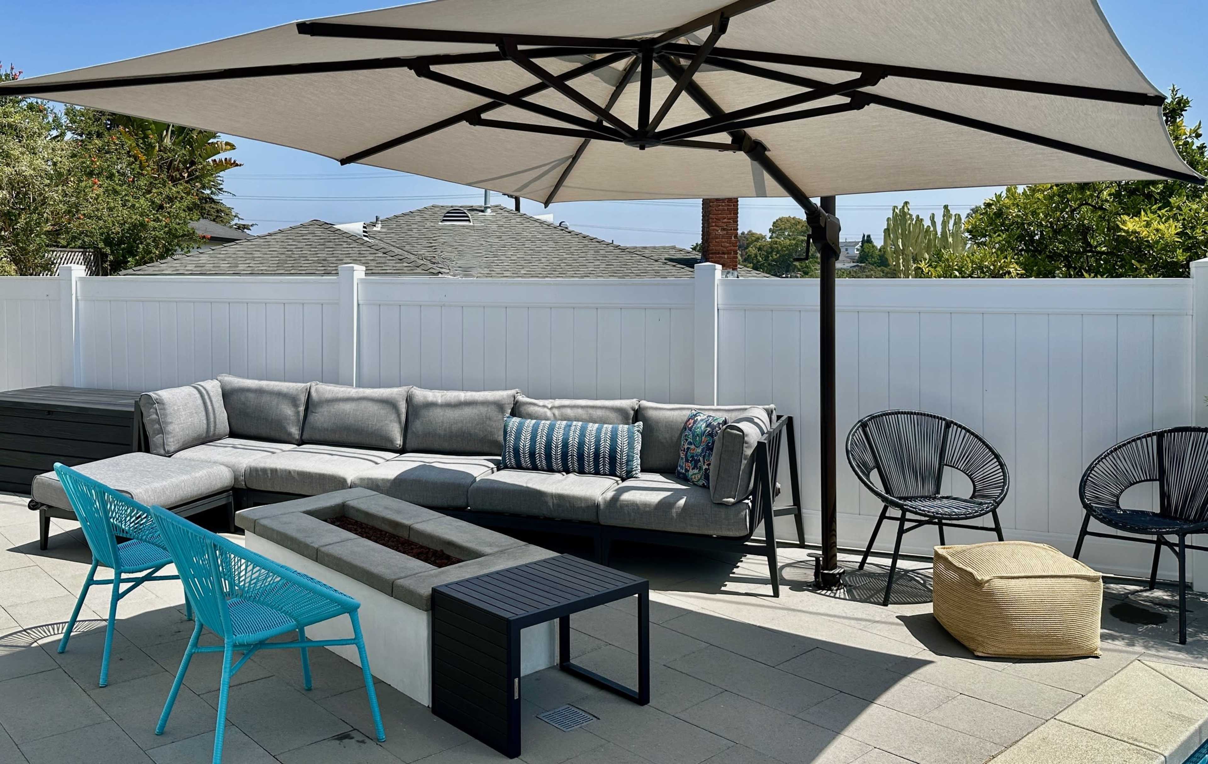 A patio features a sectional sofa under a large umbrella, a fire pit with surrounding seating, and decorative chairs.