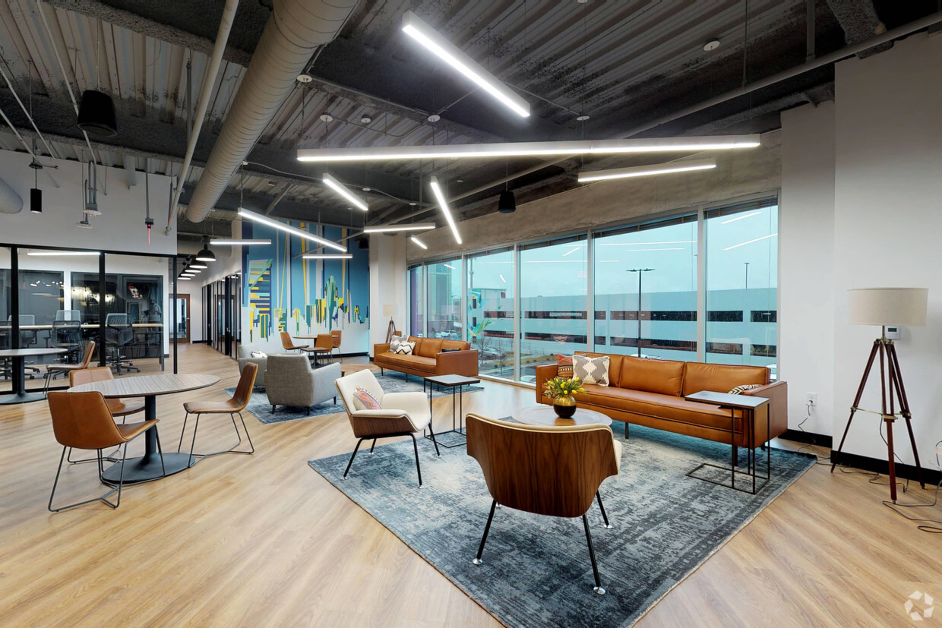 A modern office lounge area with a brown leather sofa, stylish chairs, and large windows providing natural light.