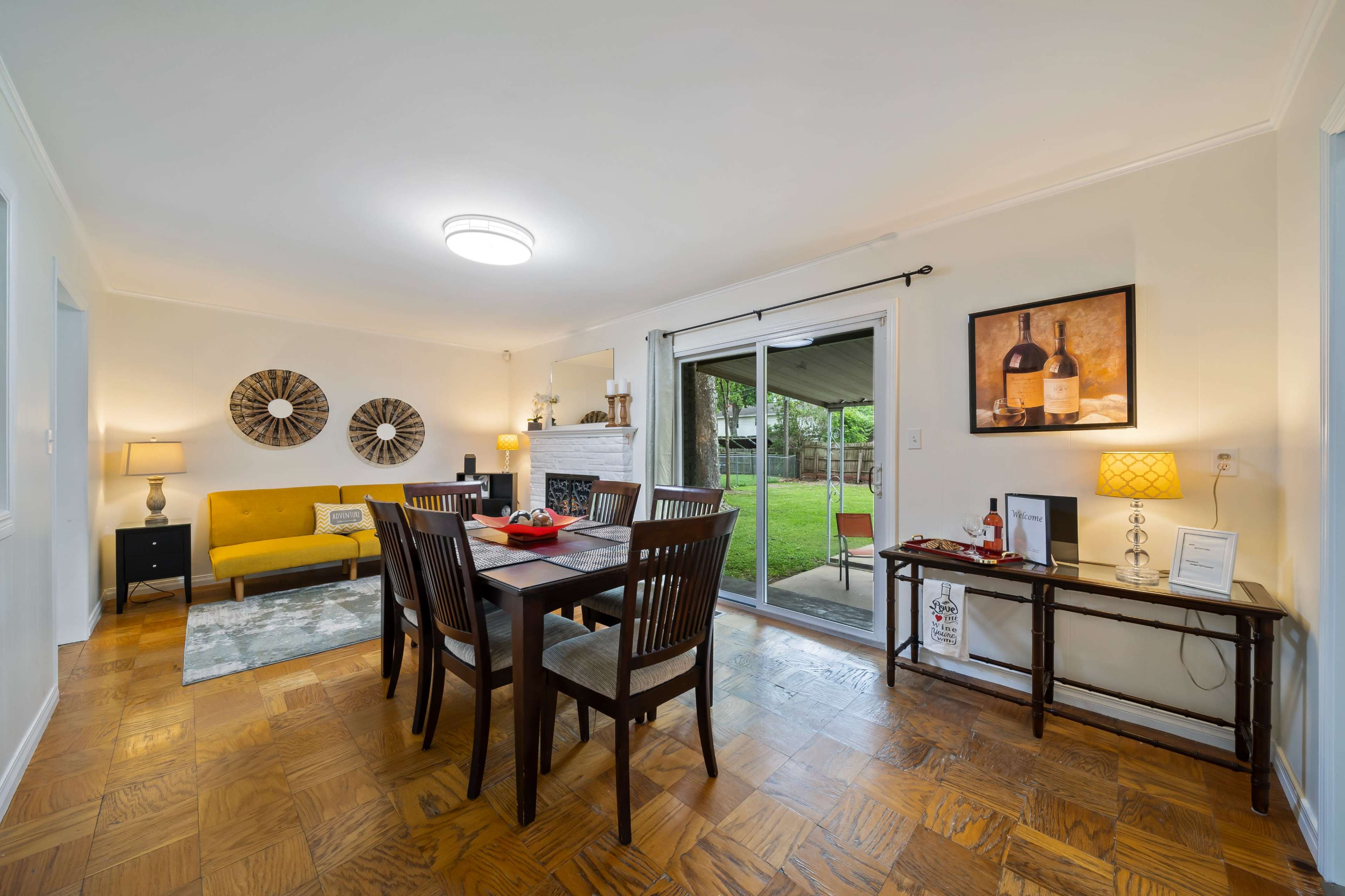 A dining area with a table and chairs, a yellow couch, and a sliding glass door leading to a backyard.
