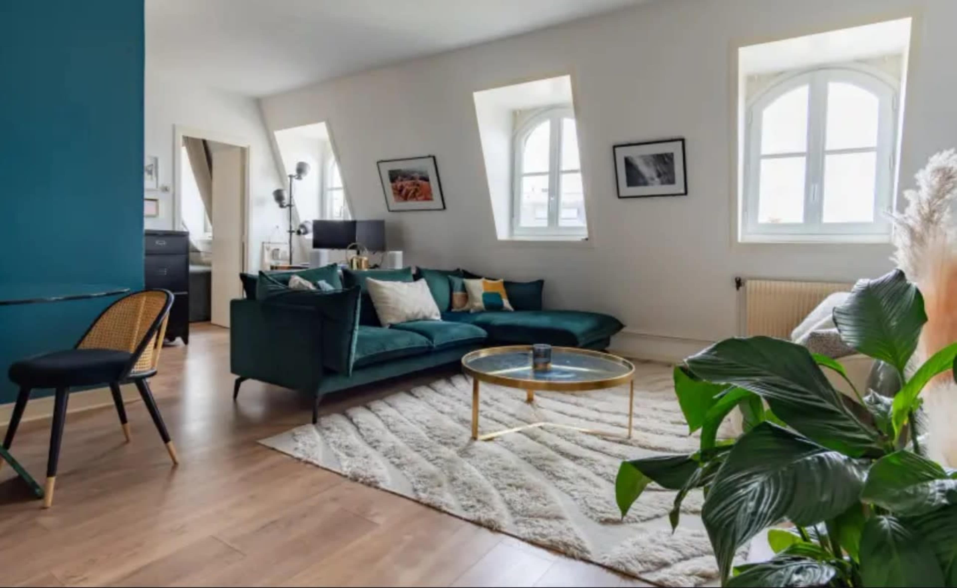 The image shows a modern living room with a green sofa, a round coffee table, and large windows that allow natural light to illuminate the space.