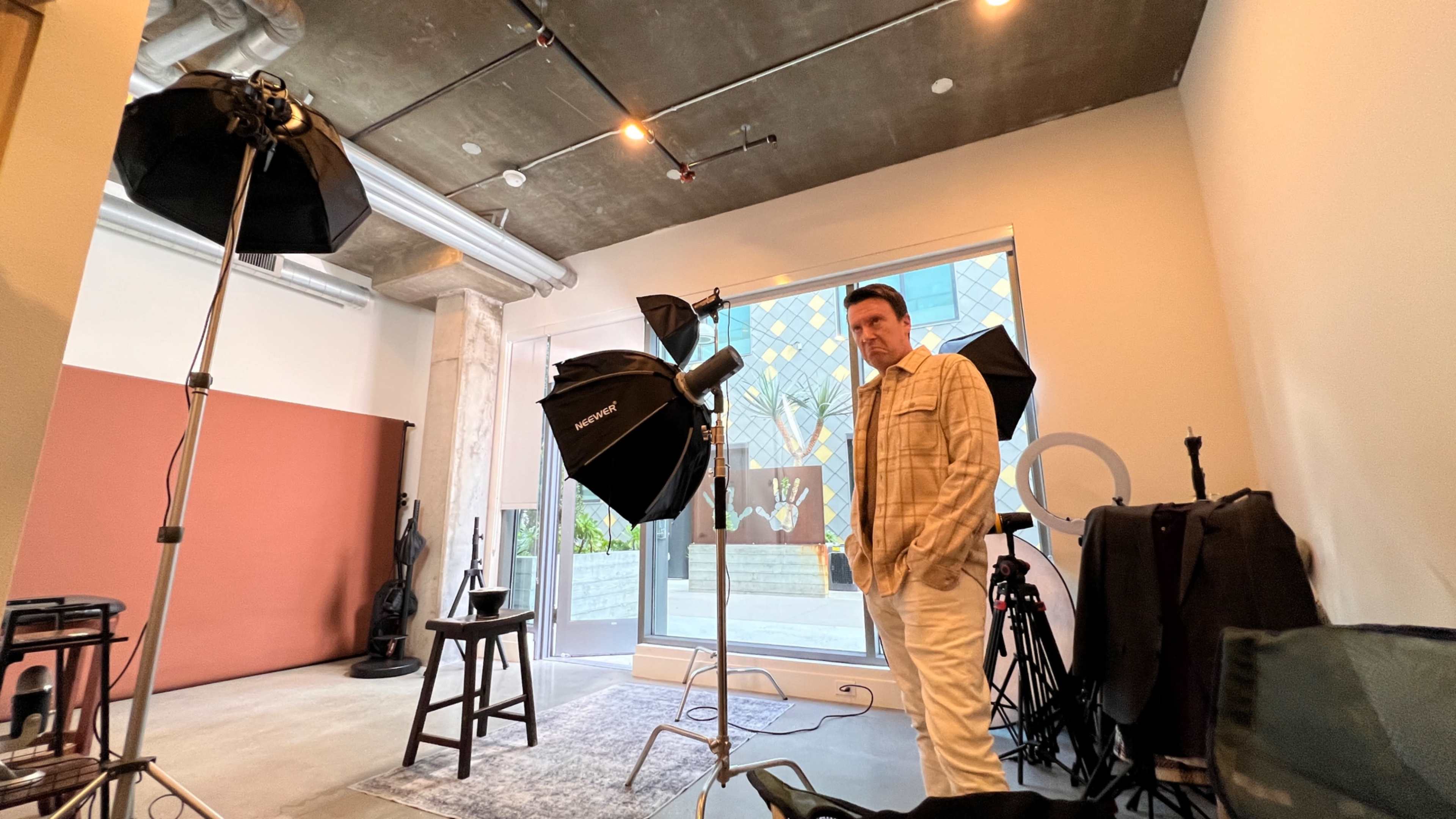 A man stands in a photography studio equipped with lights, backdrops, and seating.