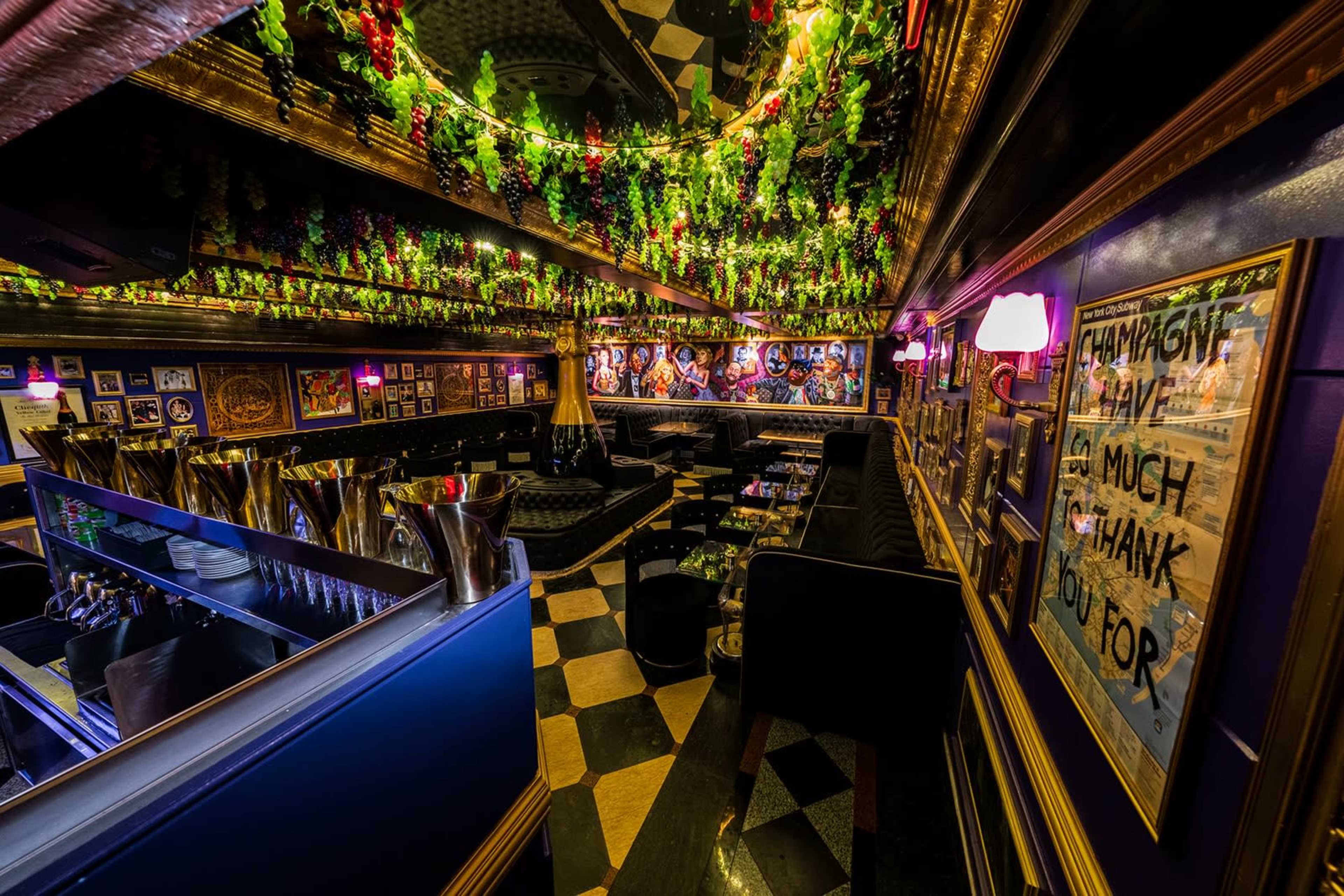 The image shows an elegantly decorated lounge with dark walls adorned with framed artwork and a ceiling covered in green foliage and lights.
