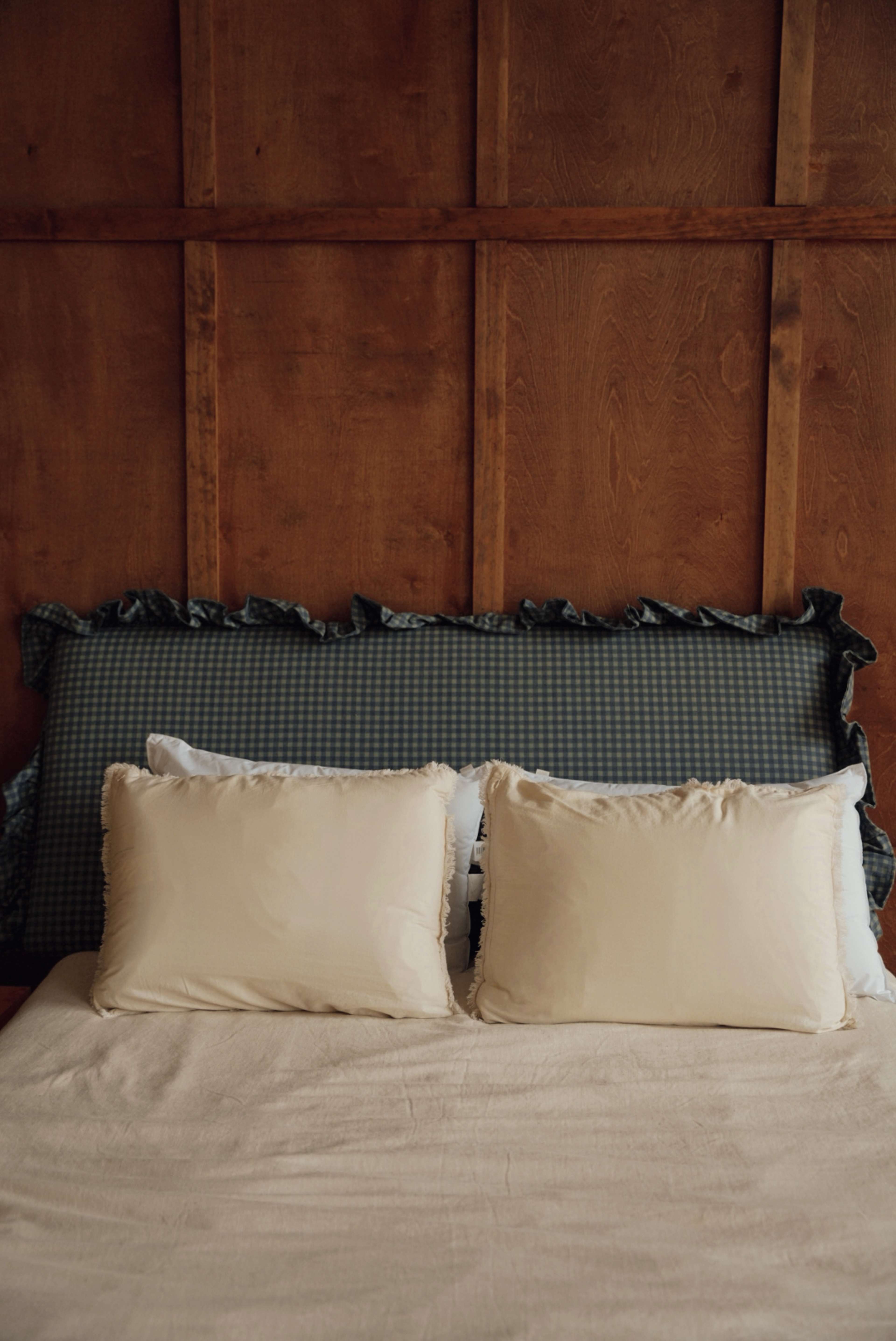 A bed with a light-colored blanket and two white pillows is positioned against a wooden paneled wall.