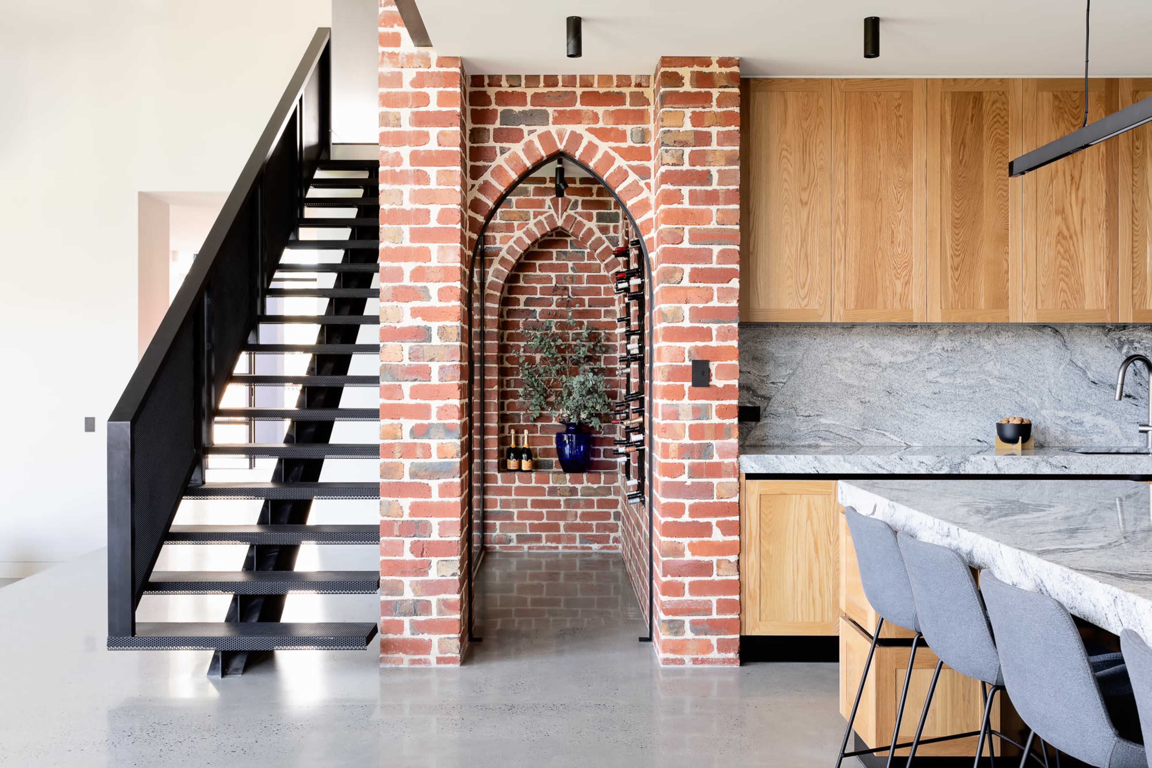 A modern kitchen with a brick archway and a staircase leading to an upper level.